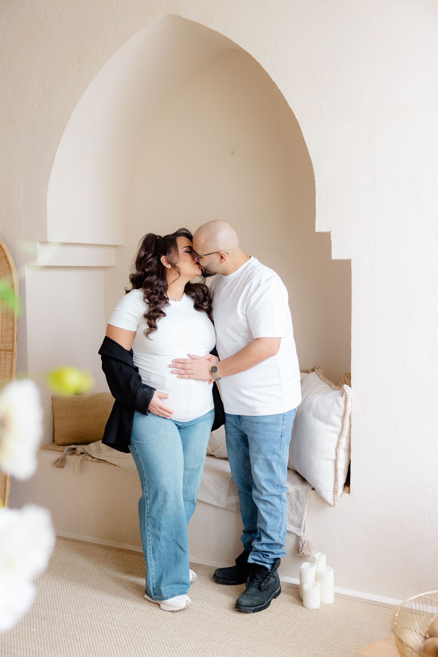 A romantic moment between a couple wearing matching white shirts and jeans standing in an arched doorway.