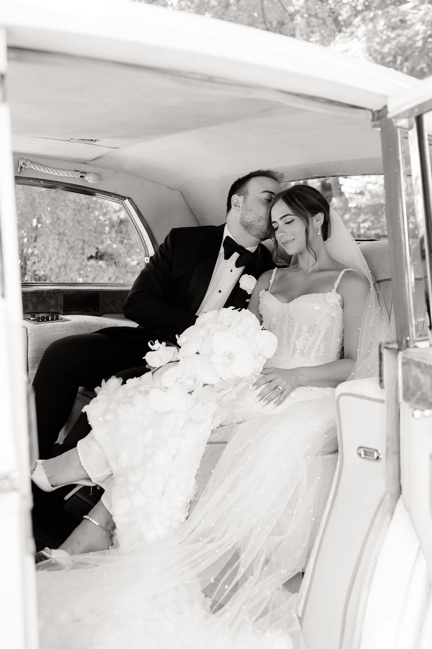 A tender romantic moment shared by newlyweds in the back of a classic car after their wedding ceremony.