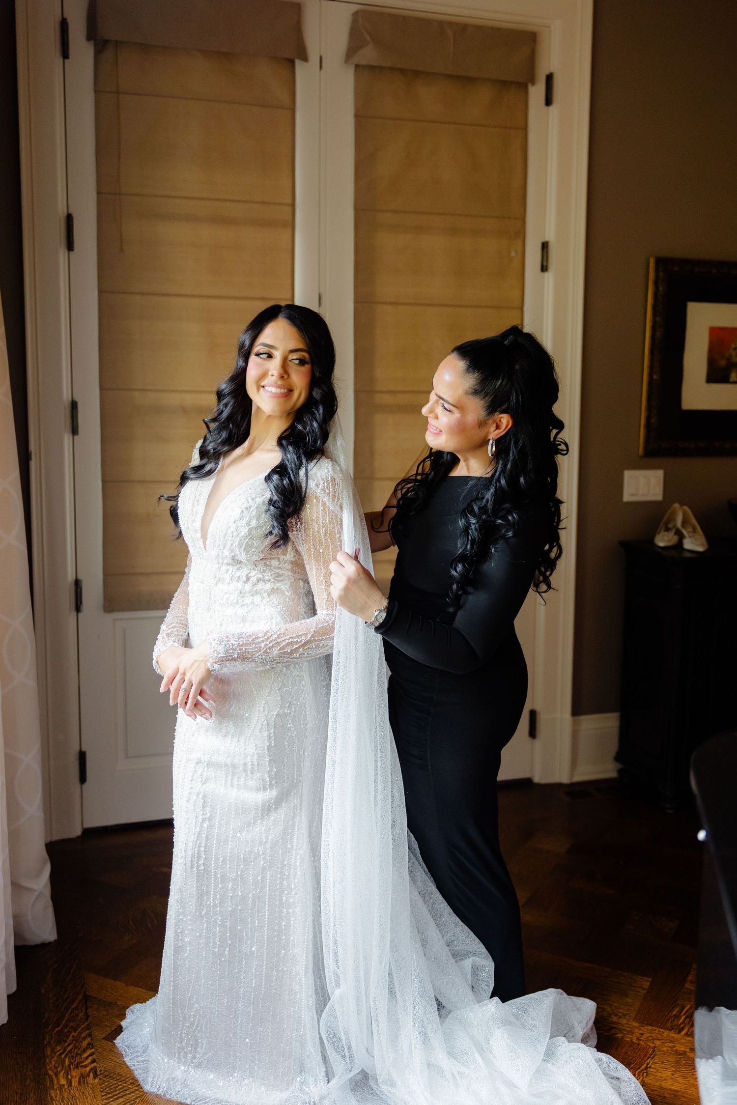 Final wedding dress adjustments in elegant room with hardwood floors and natural lighting.