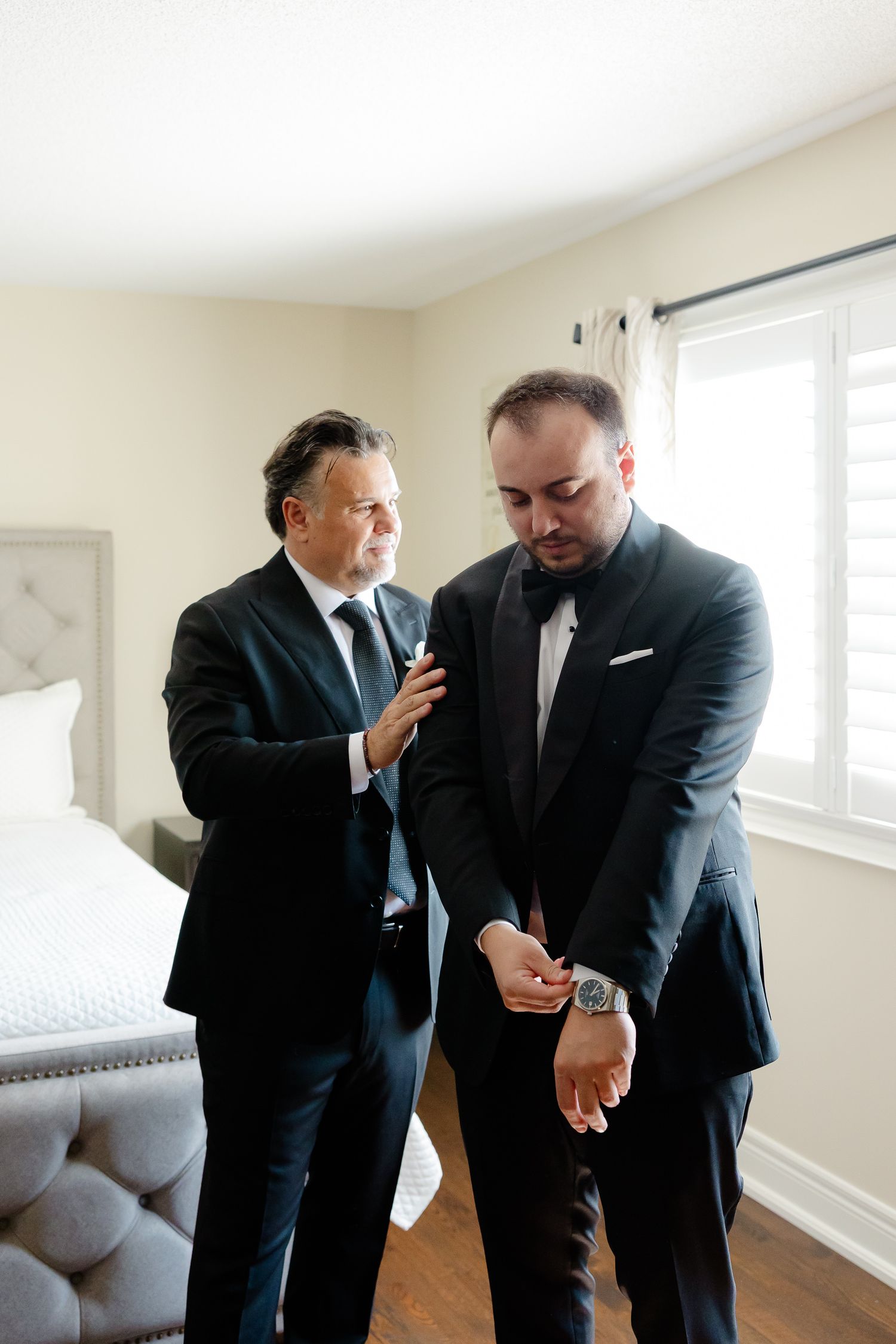Groomsmen sharing a lighthearted moment while getting dressed in formal attire for a wedding.