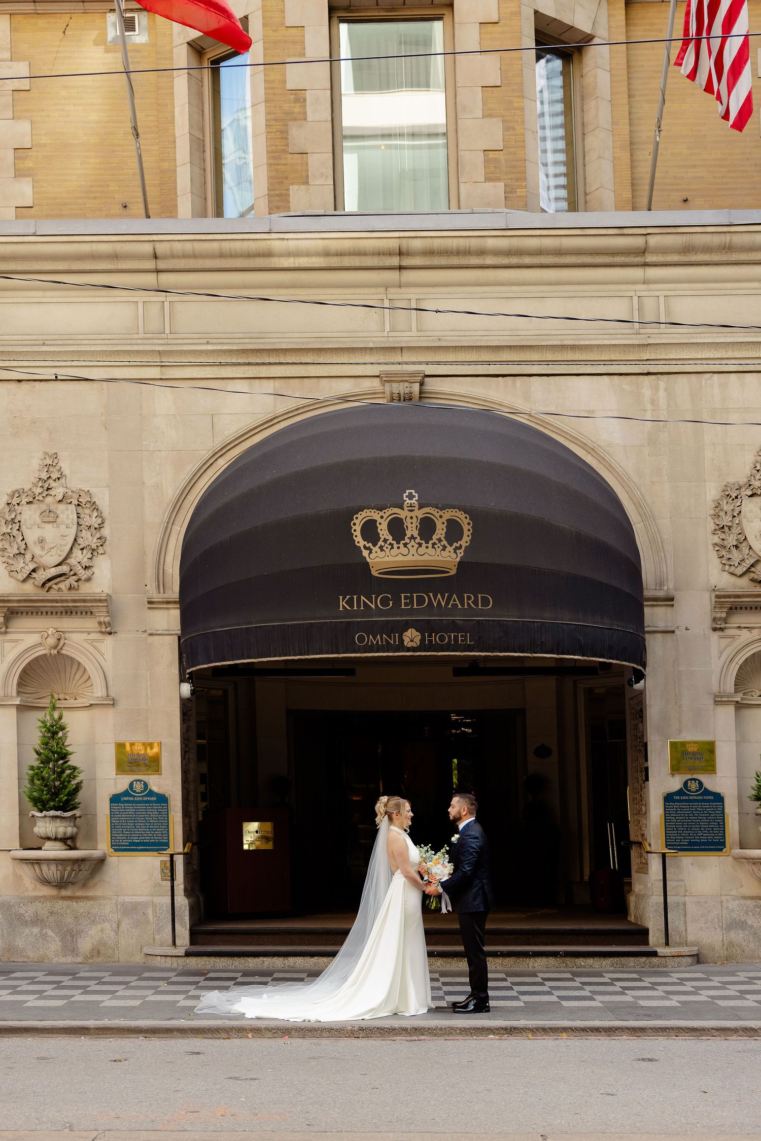 Exterior of King Edward Hotel with stone facade and black awnings featuring crown logo.