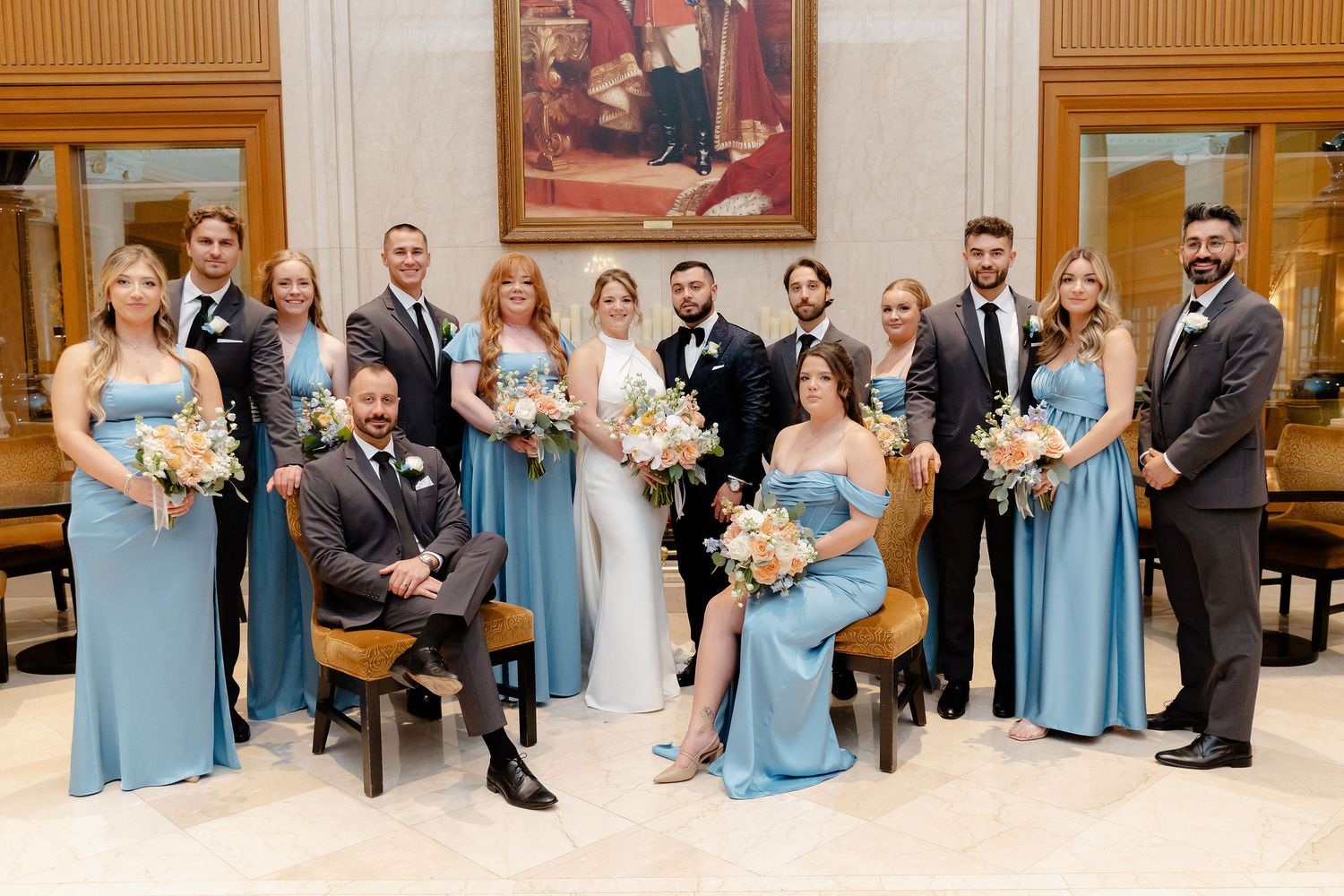 Wedding party in light blue dresses and dark suits posed in elegant indoor venue.