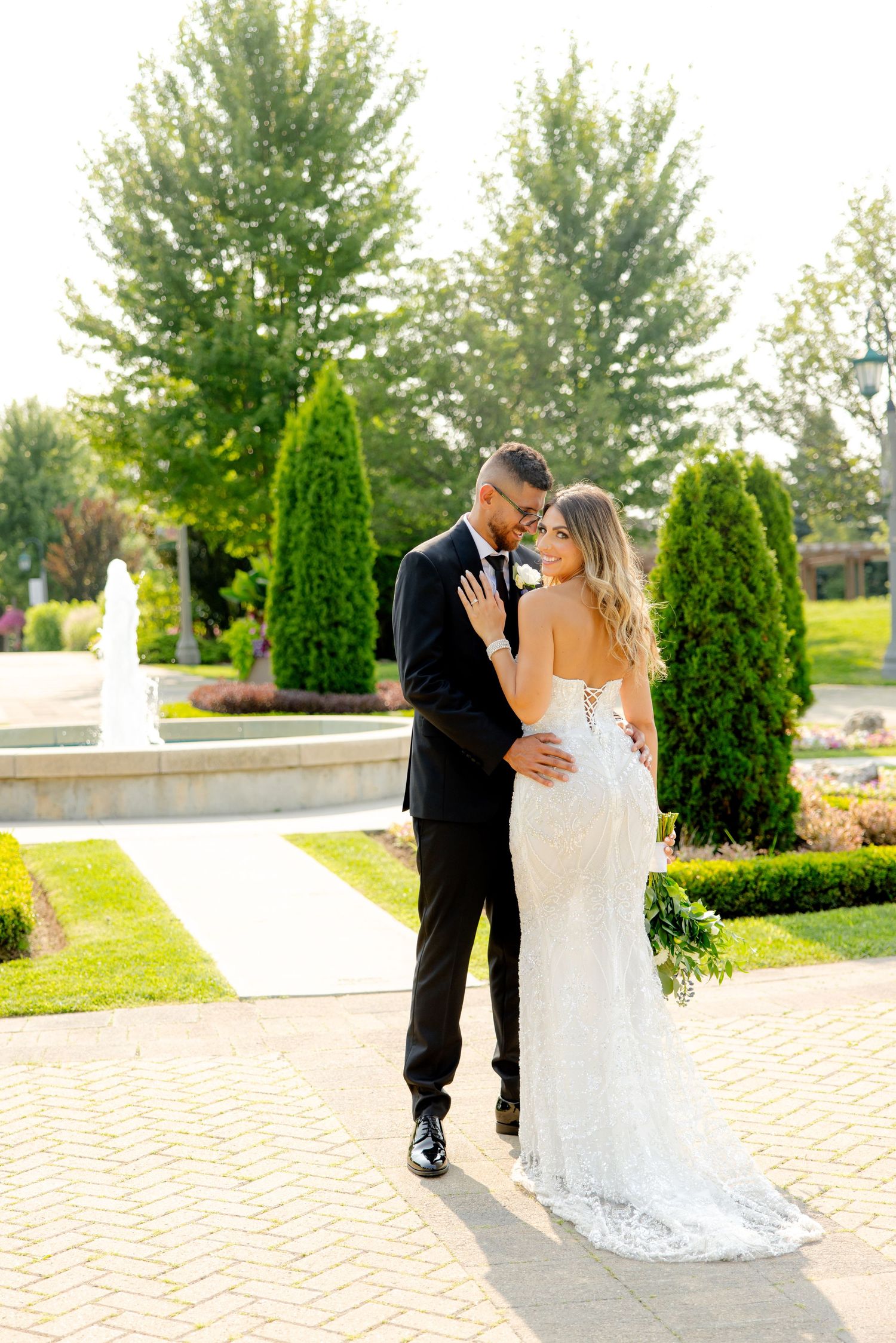 Intimate moment between newlyweds on a brick paved garden path with elegant landscaping in background.