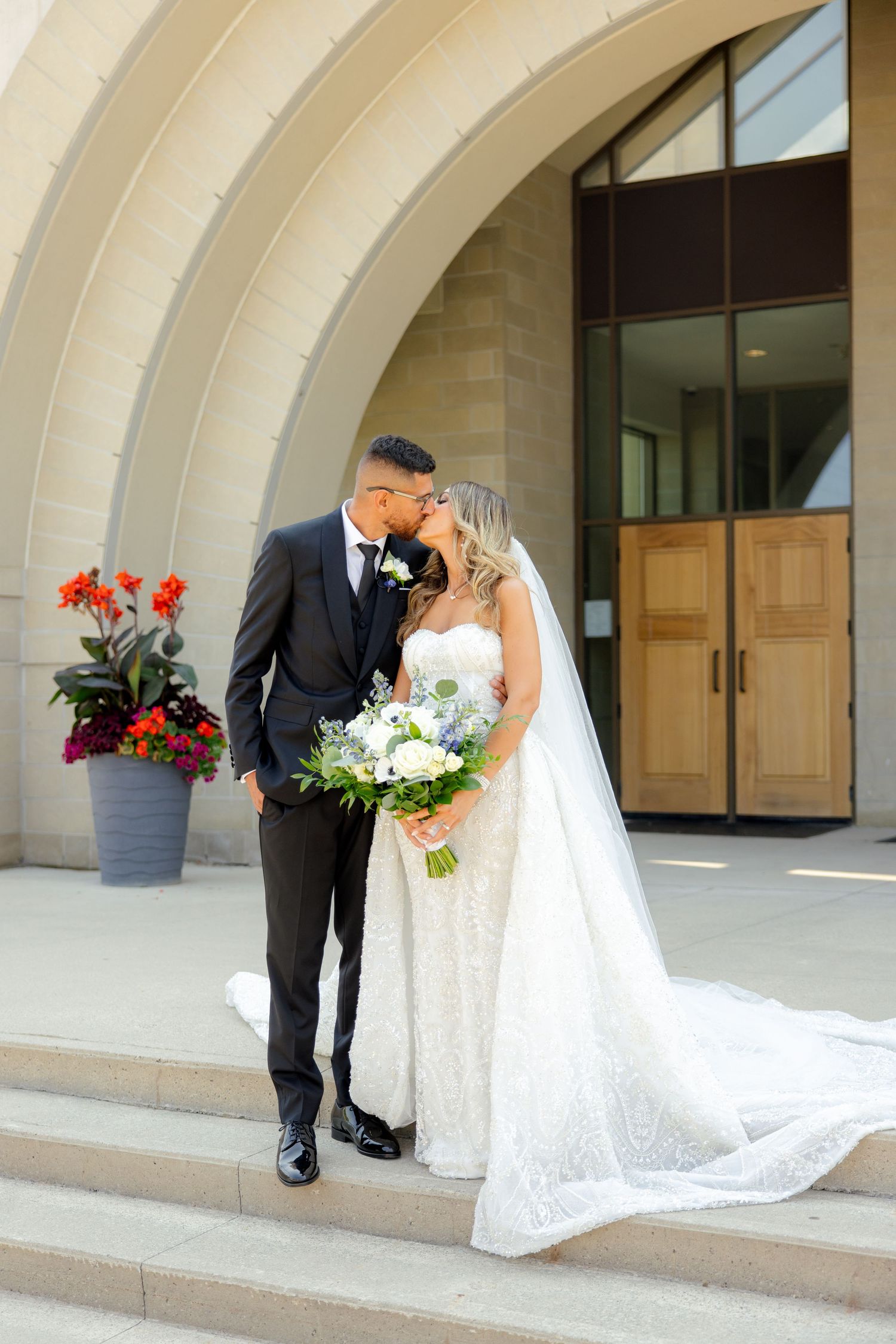 Intimate wedding moment captured under curved architectural detail with wooden doors.
