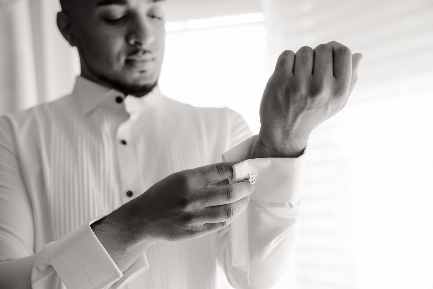 Close-up shot of hands adjusting dress shirt cuffs in natural window light.