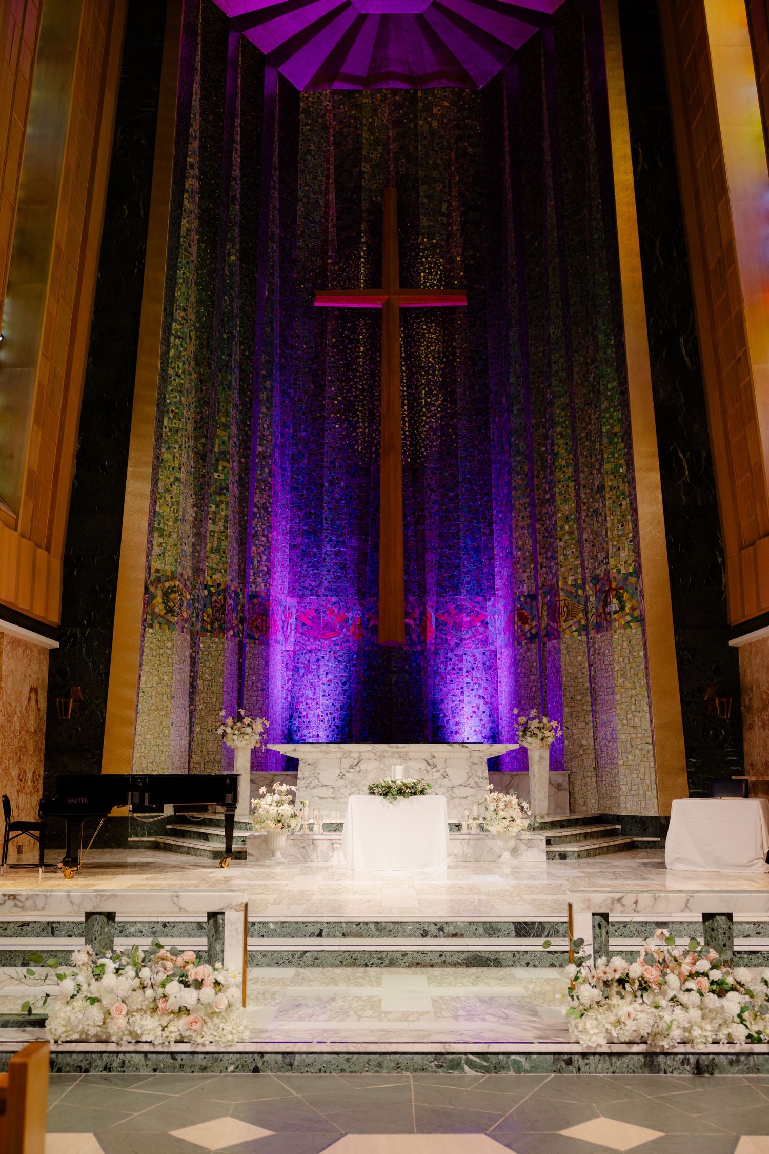 Church altar illuminated with purple lighting featuring large cross and white floral decorations.