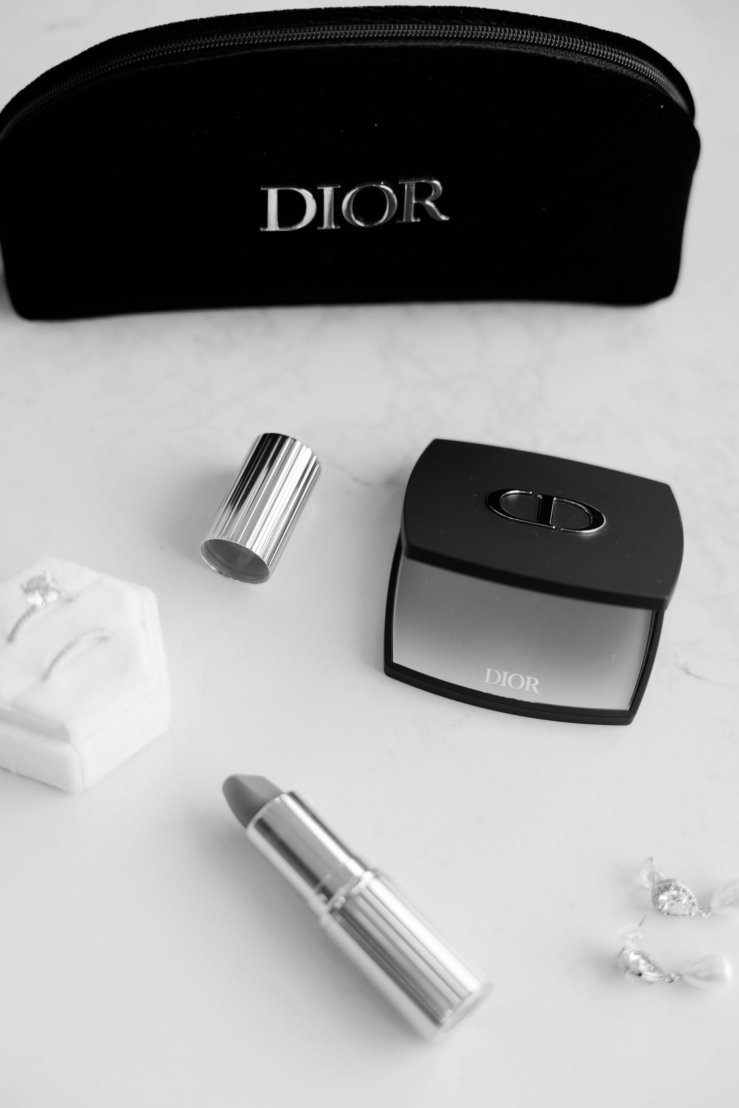 Dior cosmetics and makeup accessories arranged with black makeup bag on white surface.