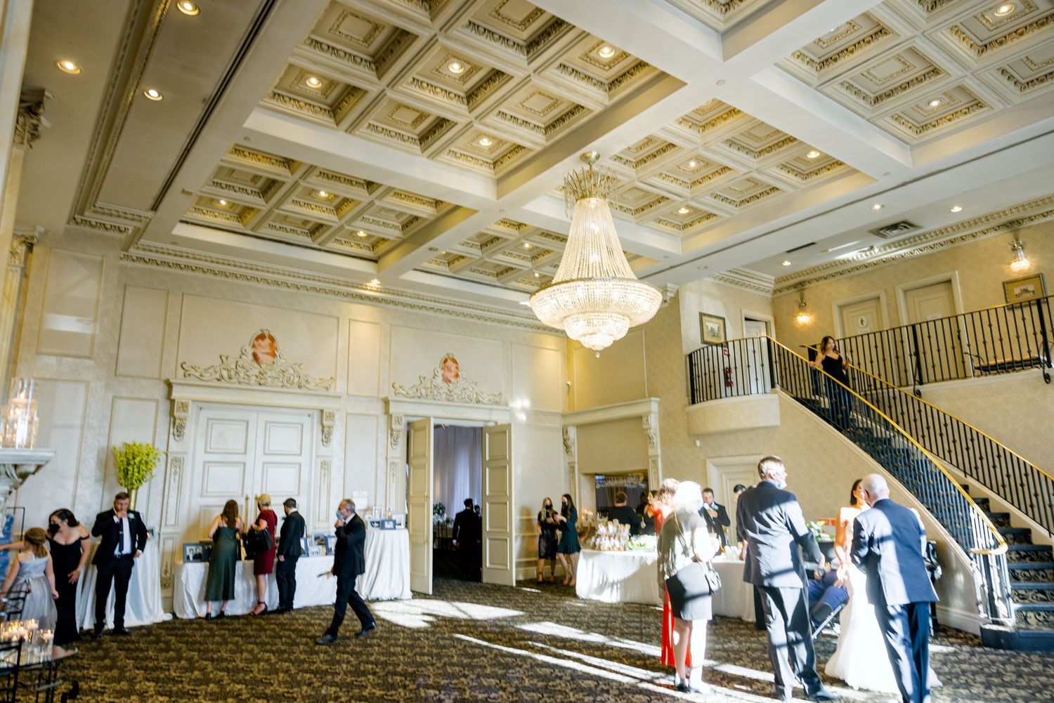 Elegant ballroom with coffered ceiling, crystal chandelier and wedding guests mingling.