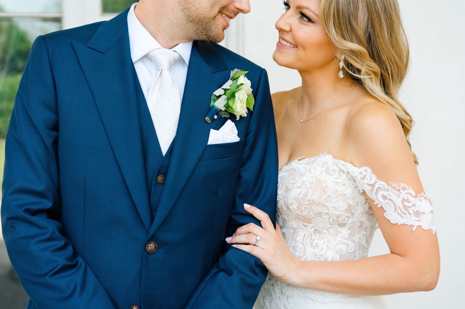 A close-up wedding portrait showcasing delicate lace details and a classic navy suit.