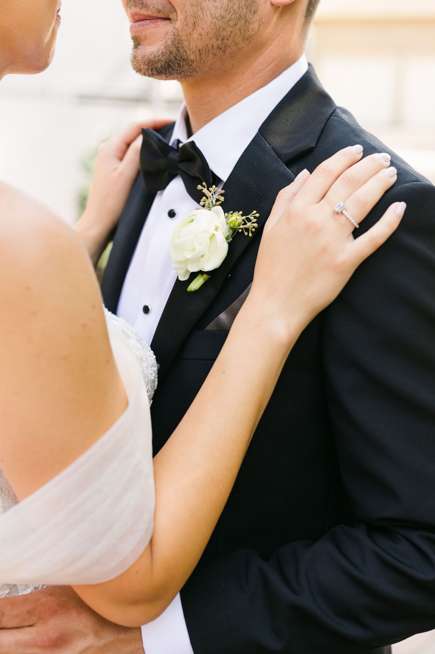 Close-up of a white boutonniere on a black tuxedo lapel with hands adjusting the collar.