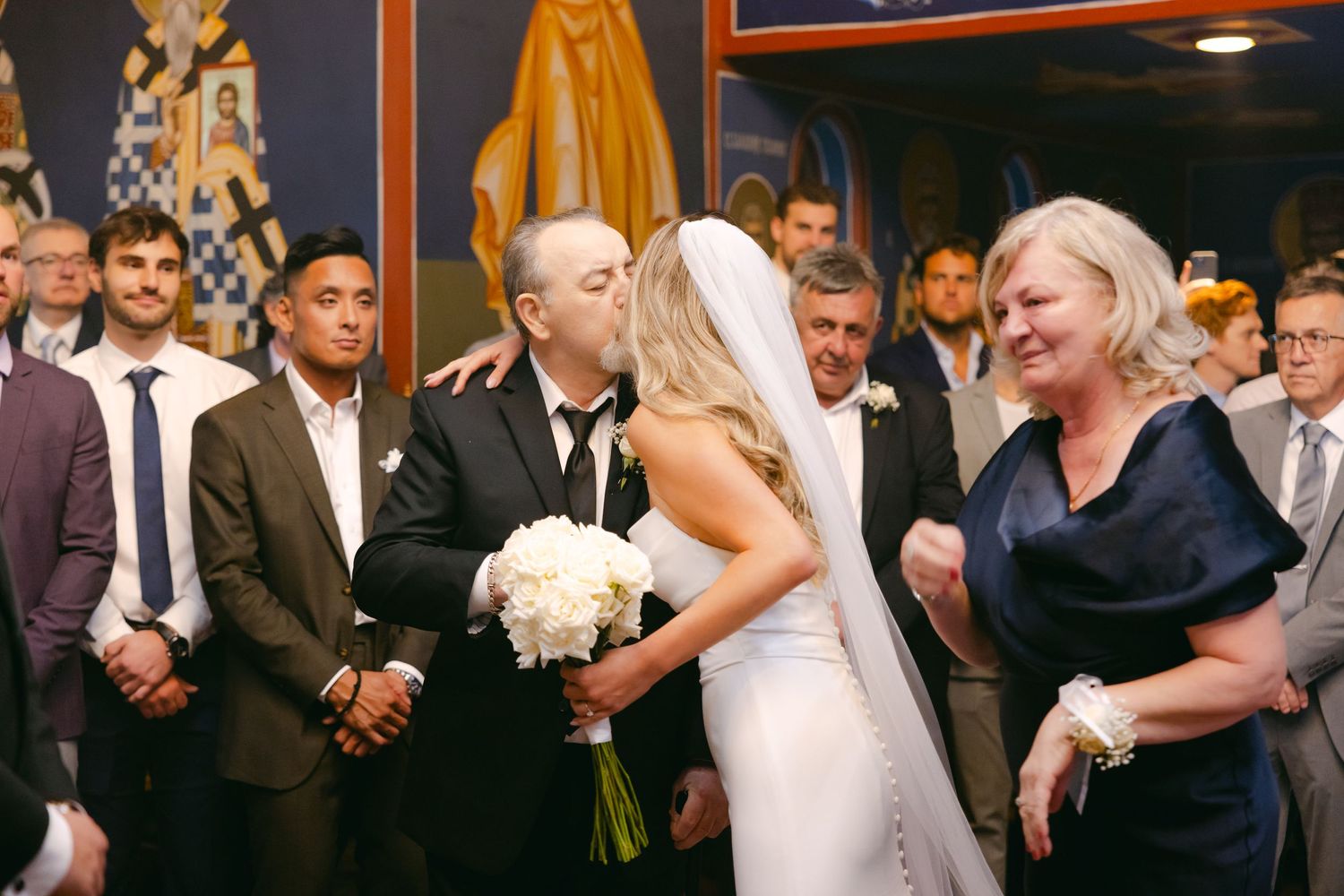 Emotional wedding ceremony moment captured inside ornately decorated venue with guests looking on.