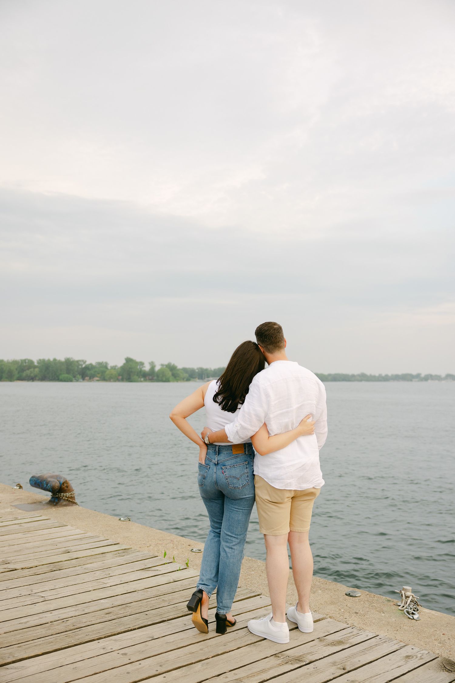Couple standing together on wooden dock overlooking peaceful waterfront view.