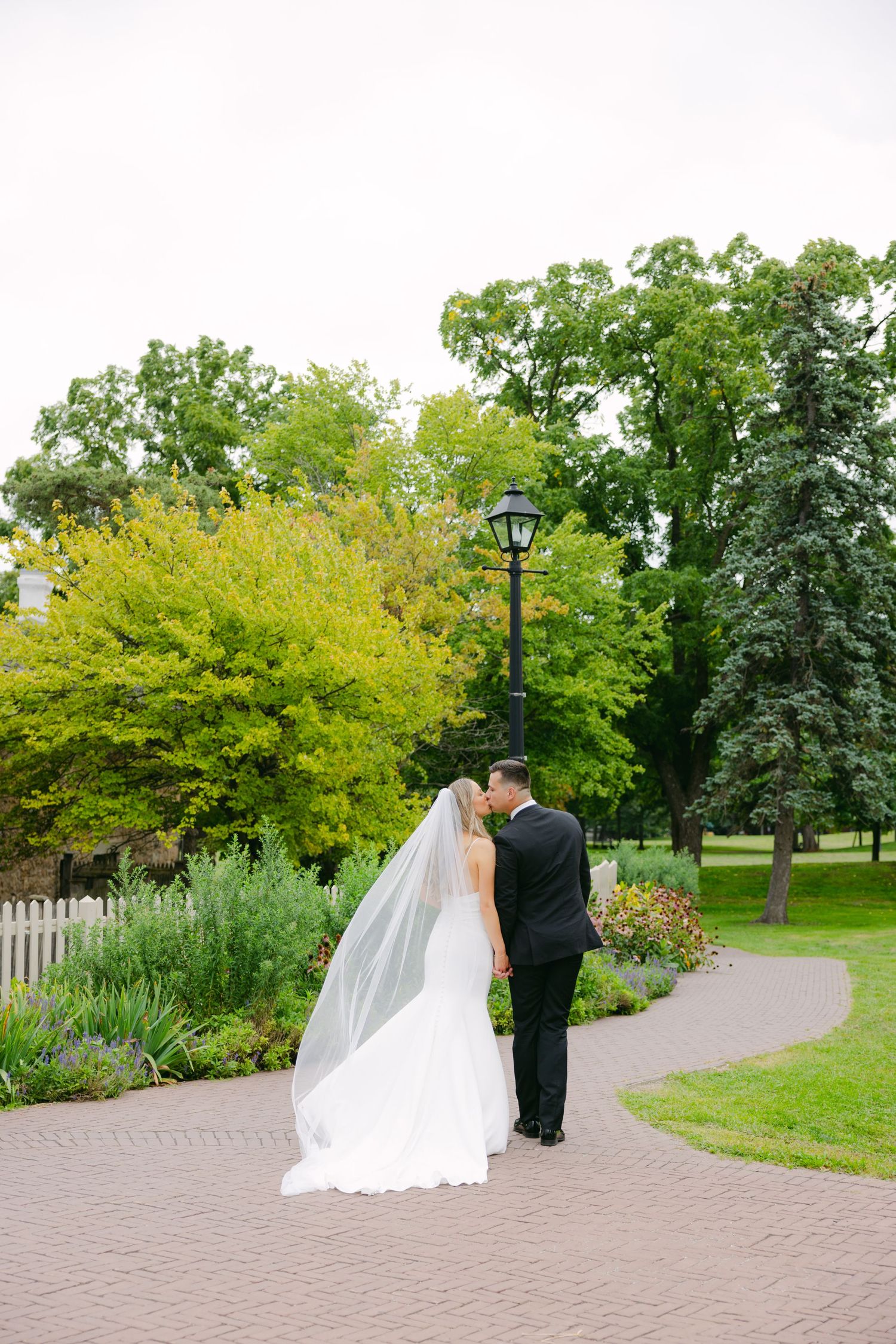 Wedding couple shares private moment on garden path near vintage lamppost and colorful foliage.