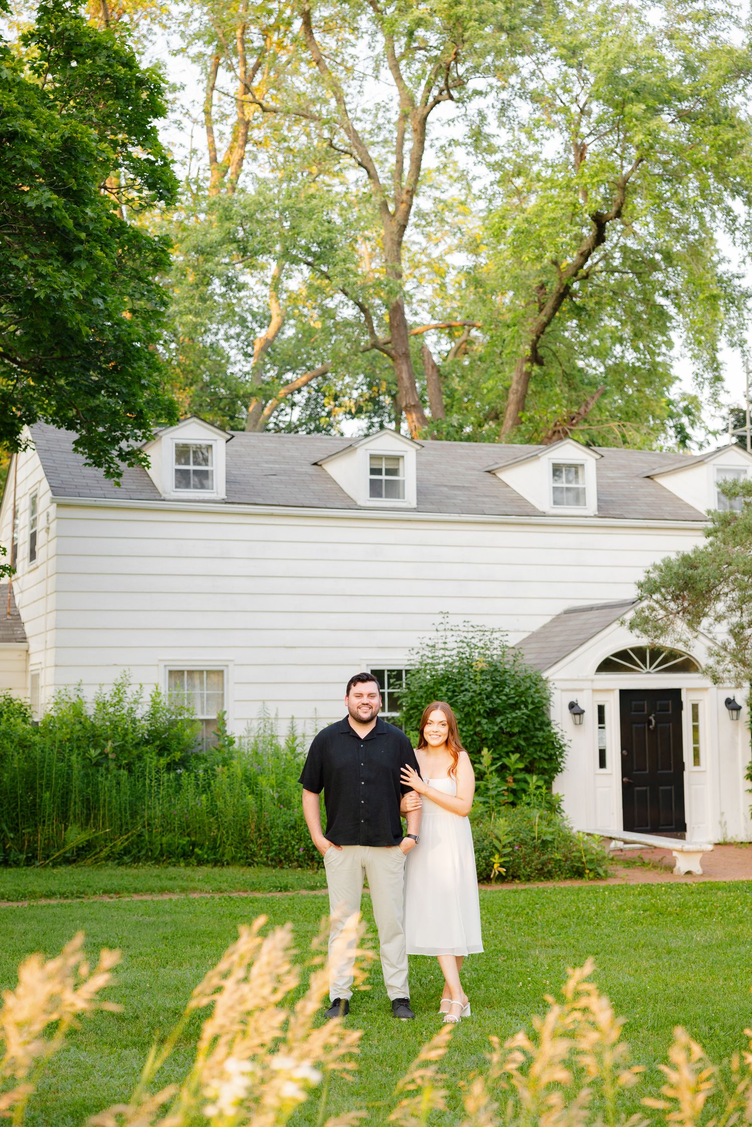 Happy couple standing together on manicured lawn with classic white house backdrop.