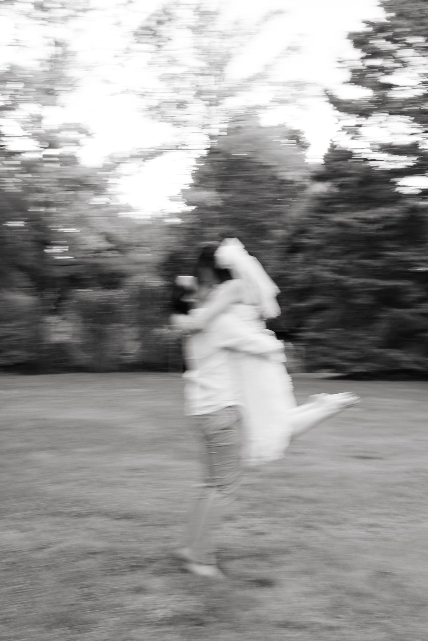 Motion-blurred black and white photo of a romantic embrace during an outdoor wedding.