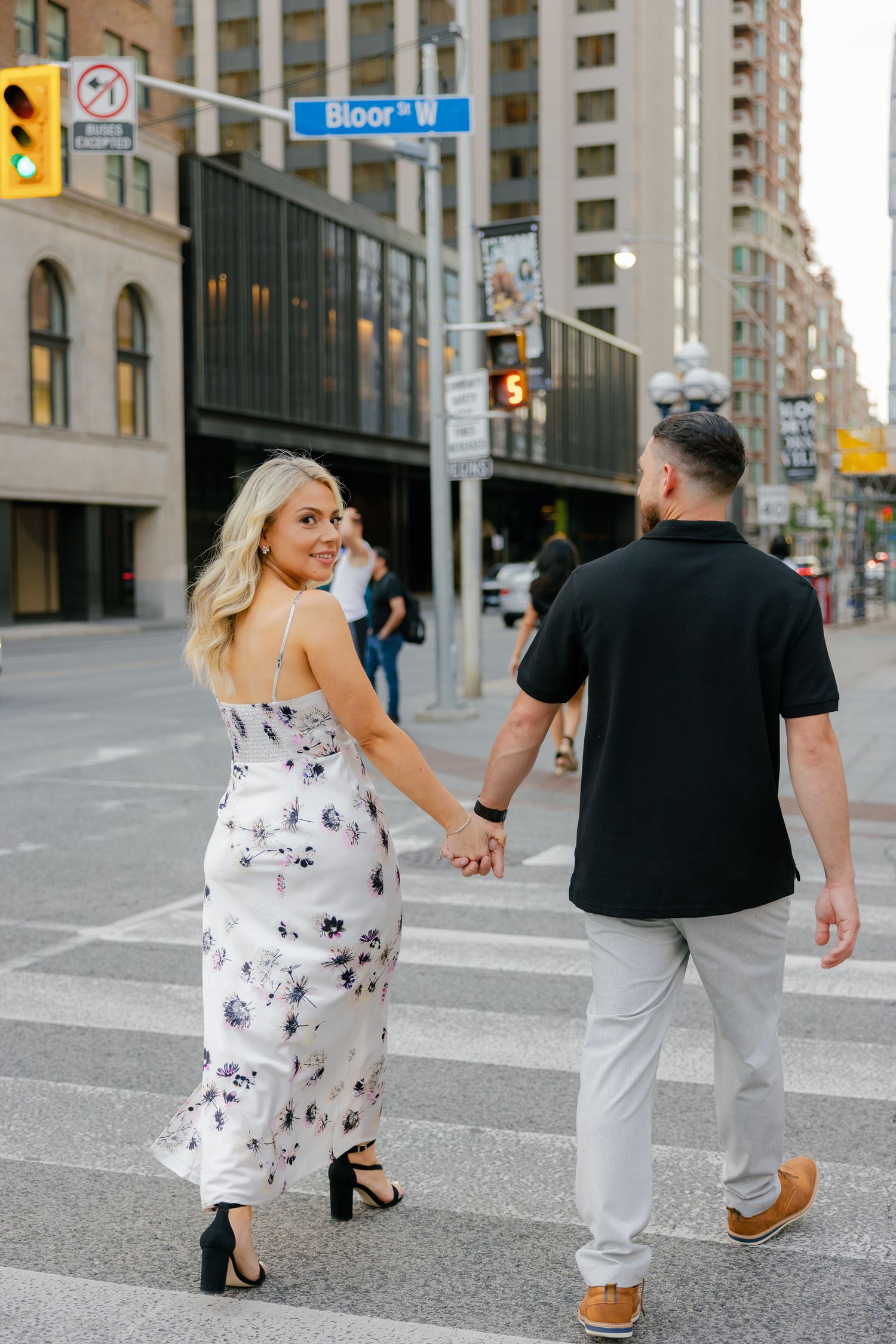 A couple crosses an urban intersection while holding hands near Bloor Street.
