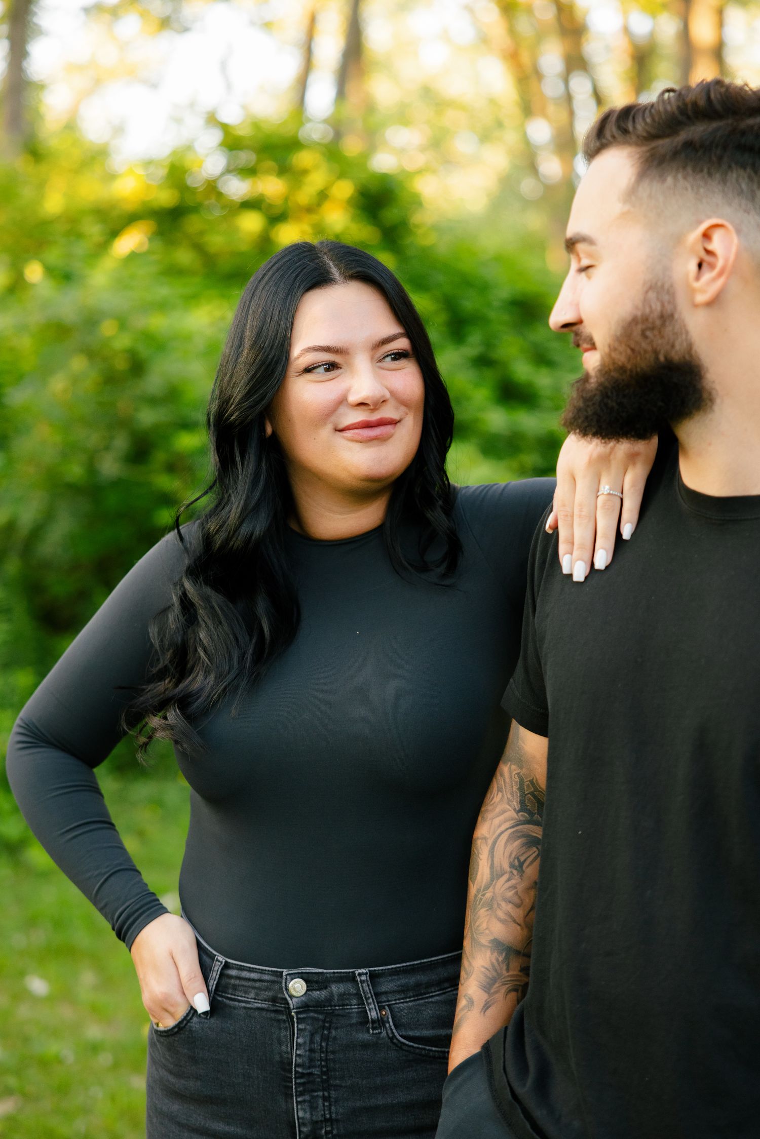 Couple in black clothing sharing intimate moment while posing against natural forest backdrop.