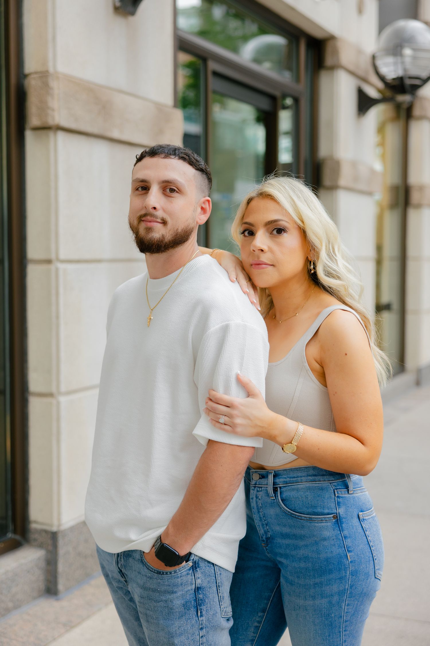 A fashionable couple in white and denim poses outside an urban storefront.