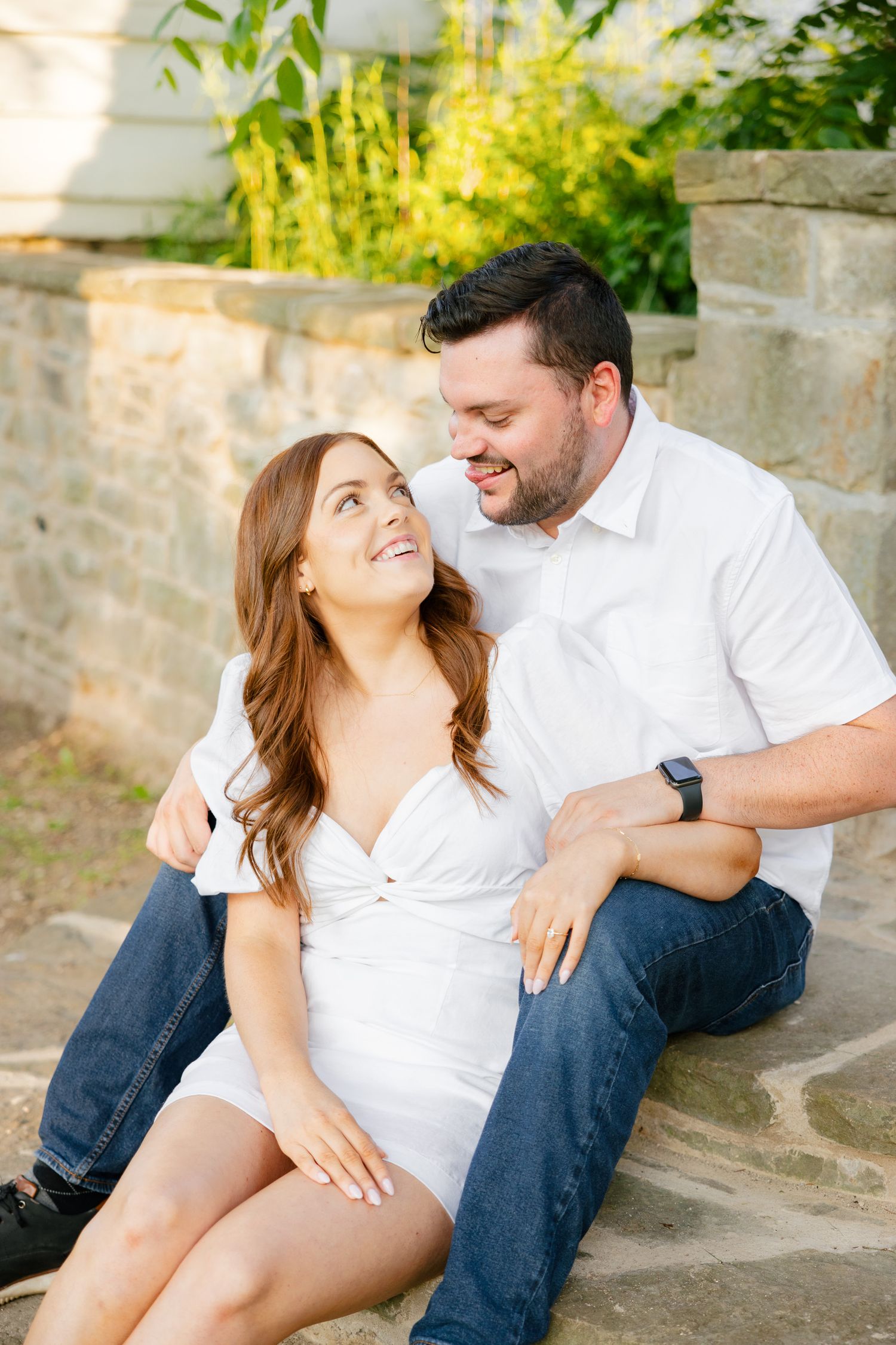 A couple shares a loving moment while sitting on stone steps in a garden setting.