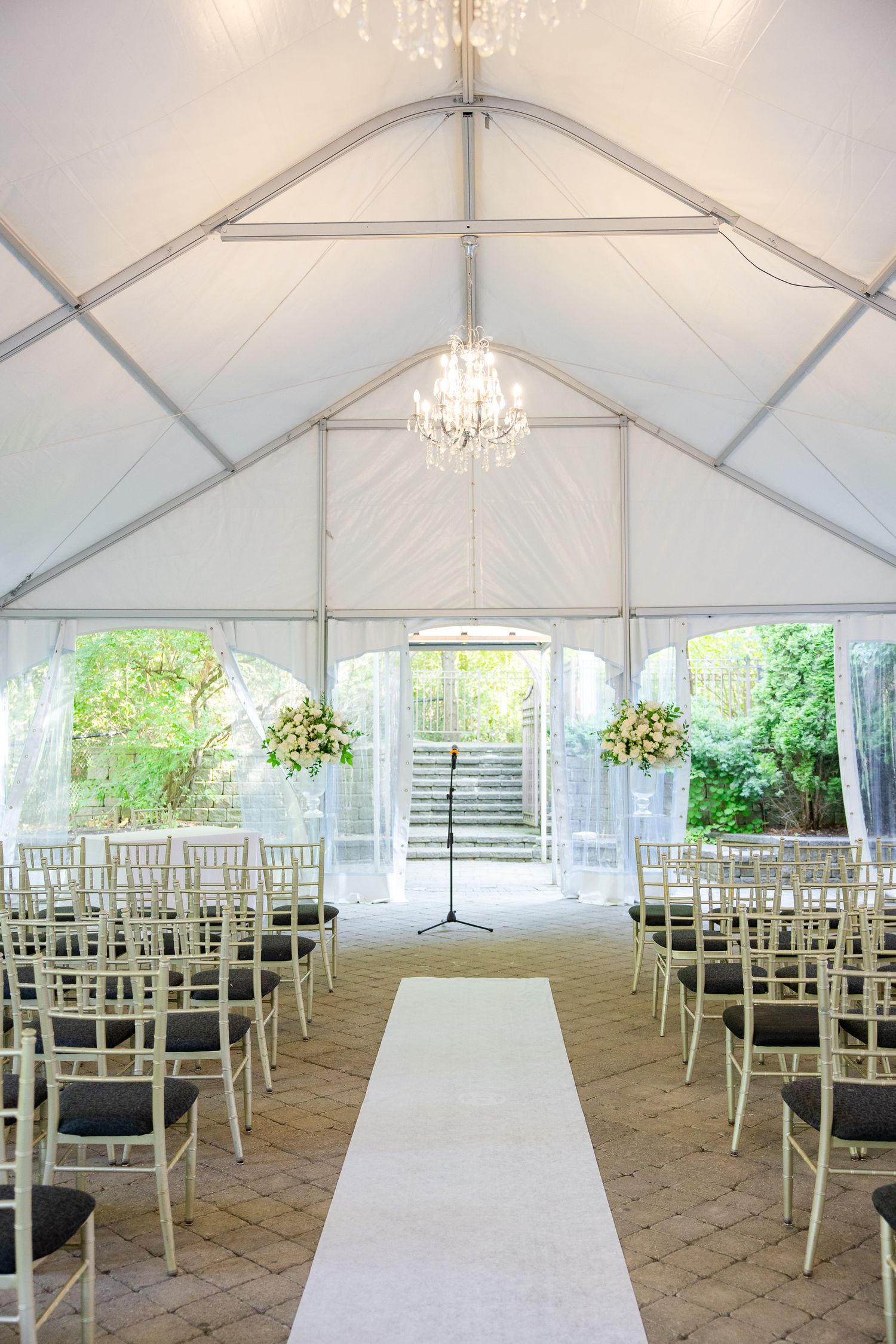 Elegant wedding ceremony setup in a white tent with crystal chandelier and rows of white chairs along a central aisle.