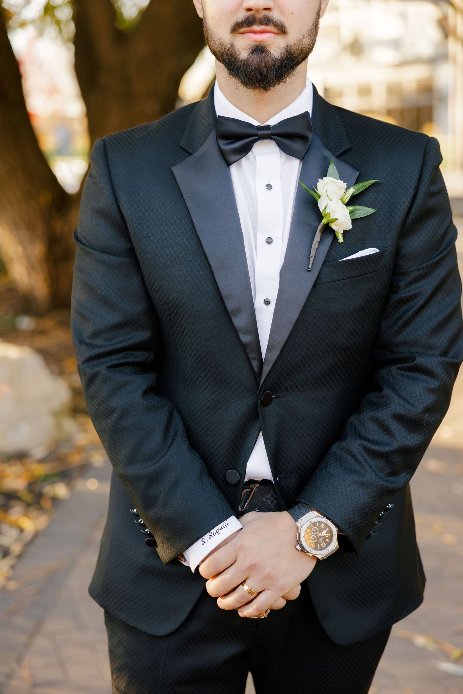 Close-up detail of groom's tuxedo with white boutonniere and bow tie.