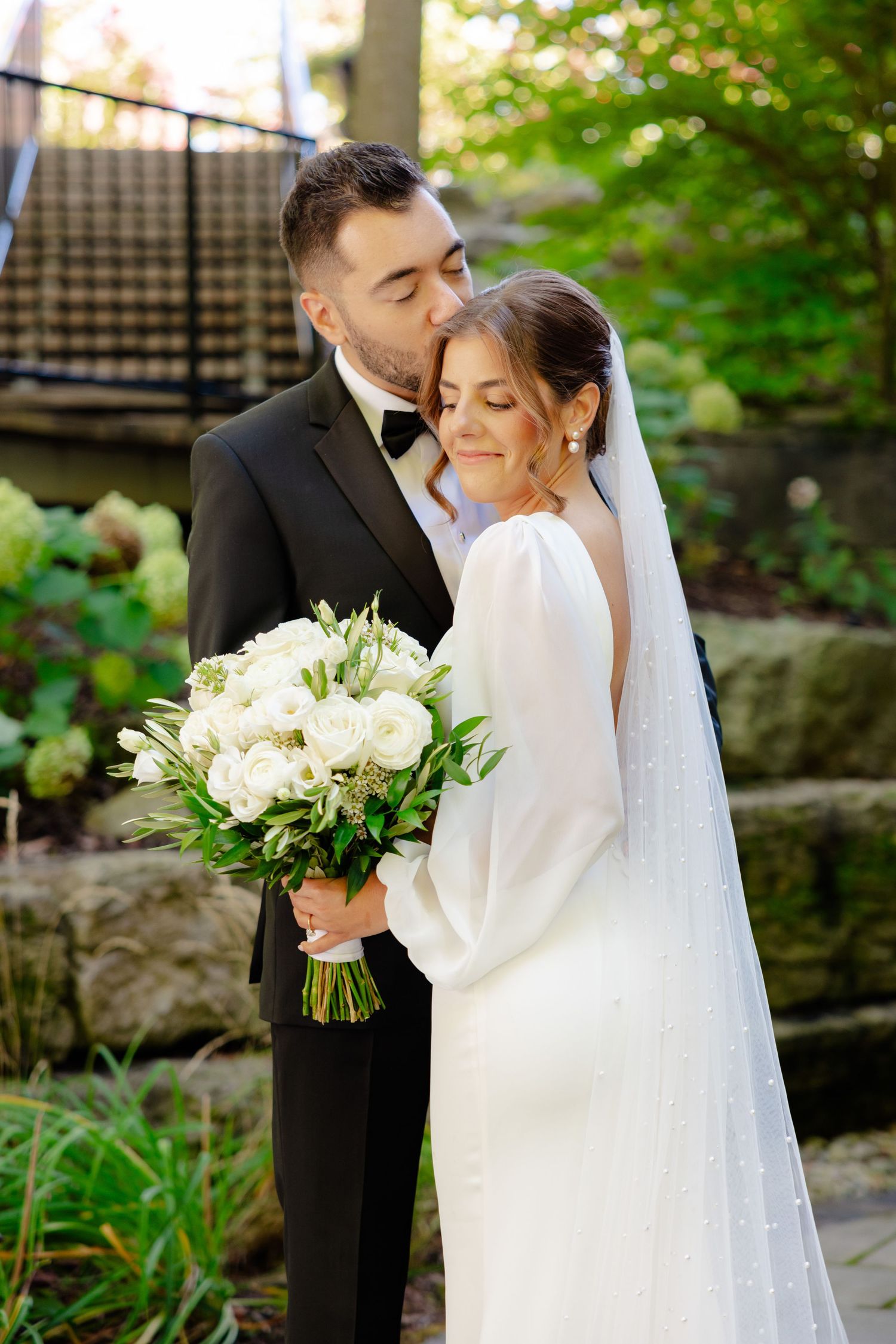 Intimate wedding moment captured outdoors with white bouquet and flowing veil.
