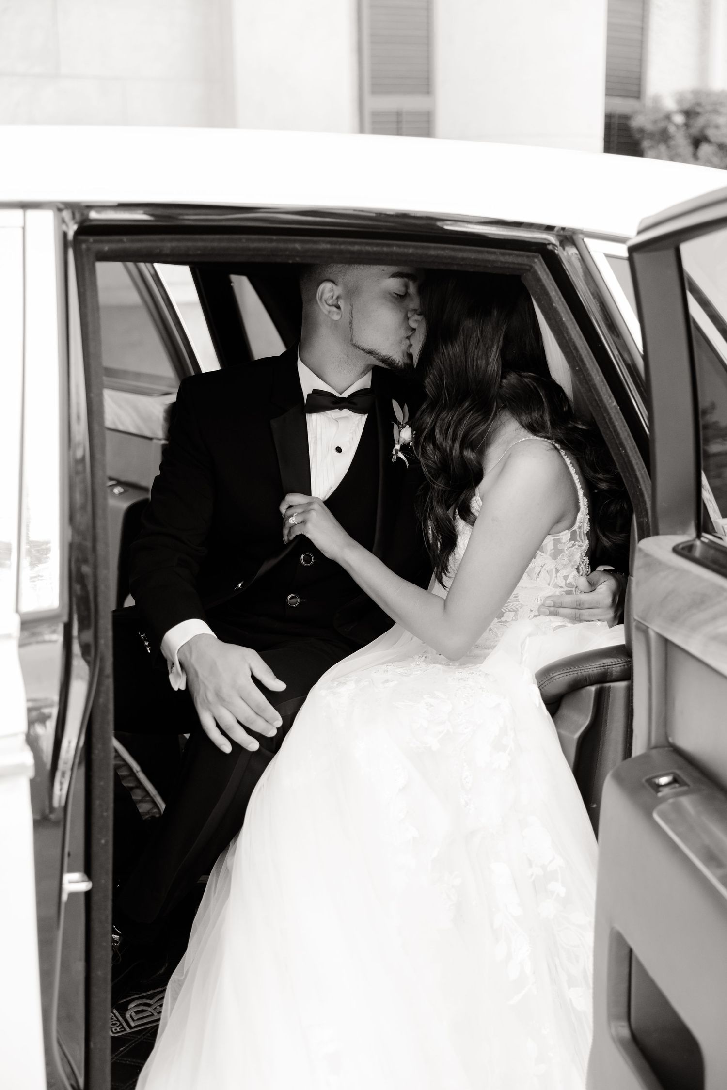 Classic black and white photo of newlyweds sharing a romantic moment in their wedding car.