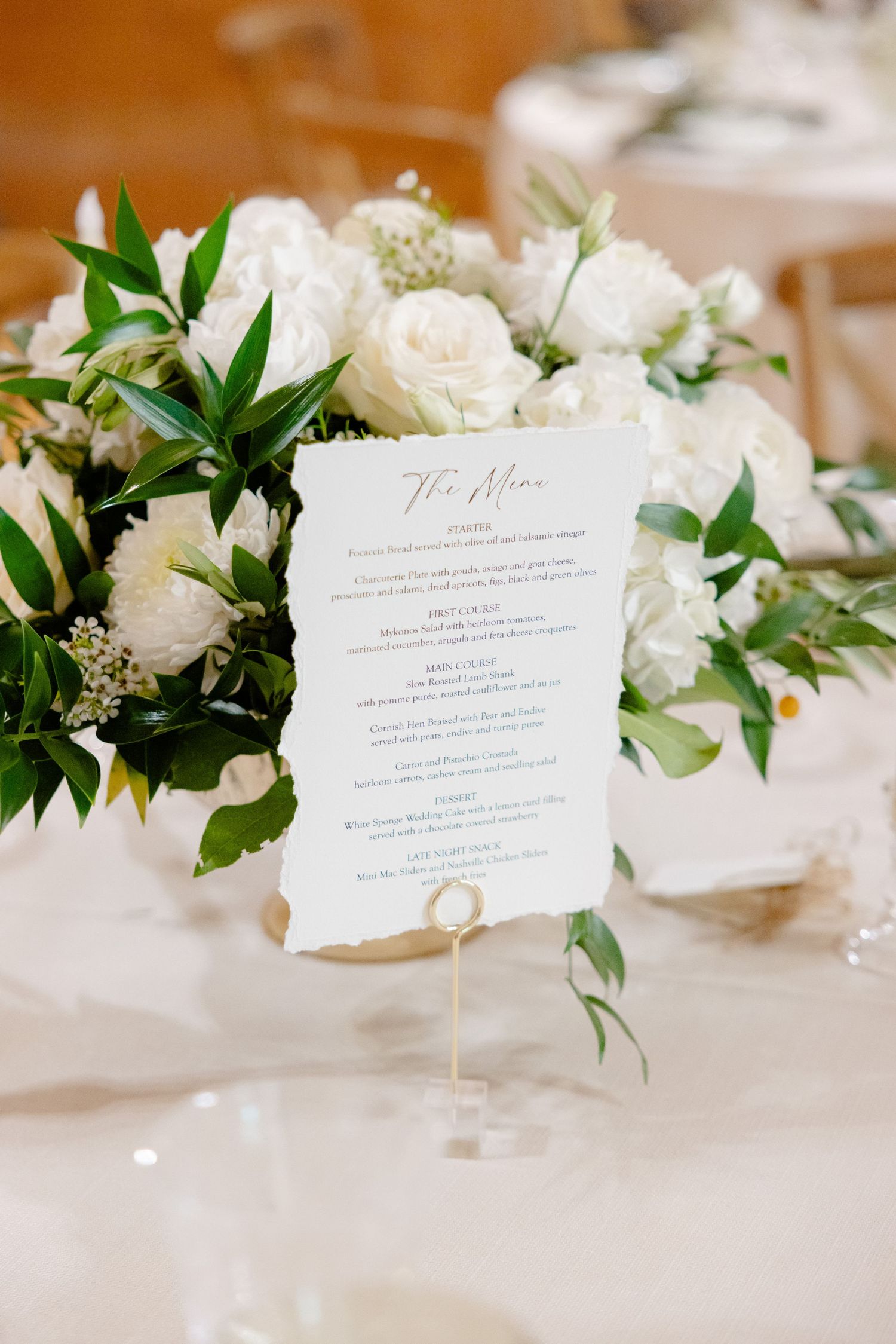 Elegant wedding menu card displayed among white roses and greenery on a table setting.