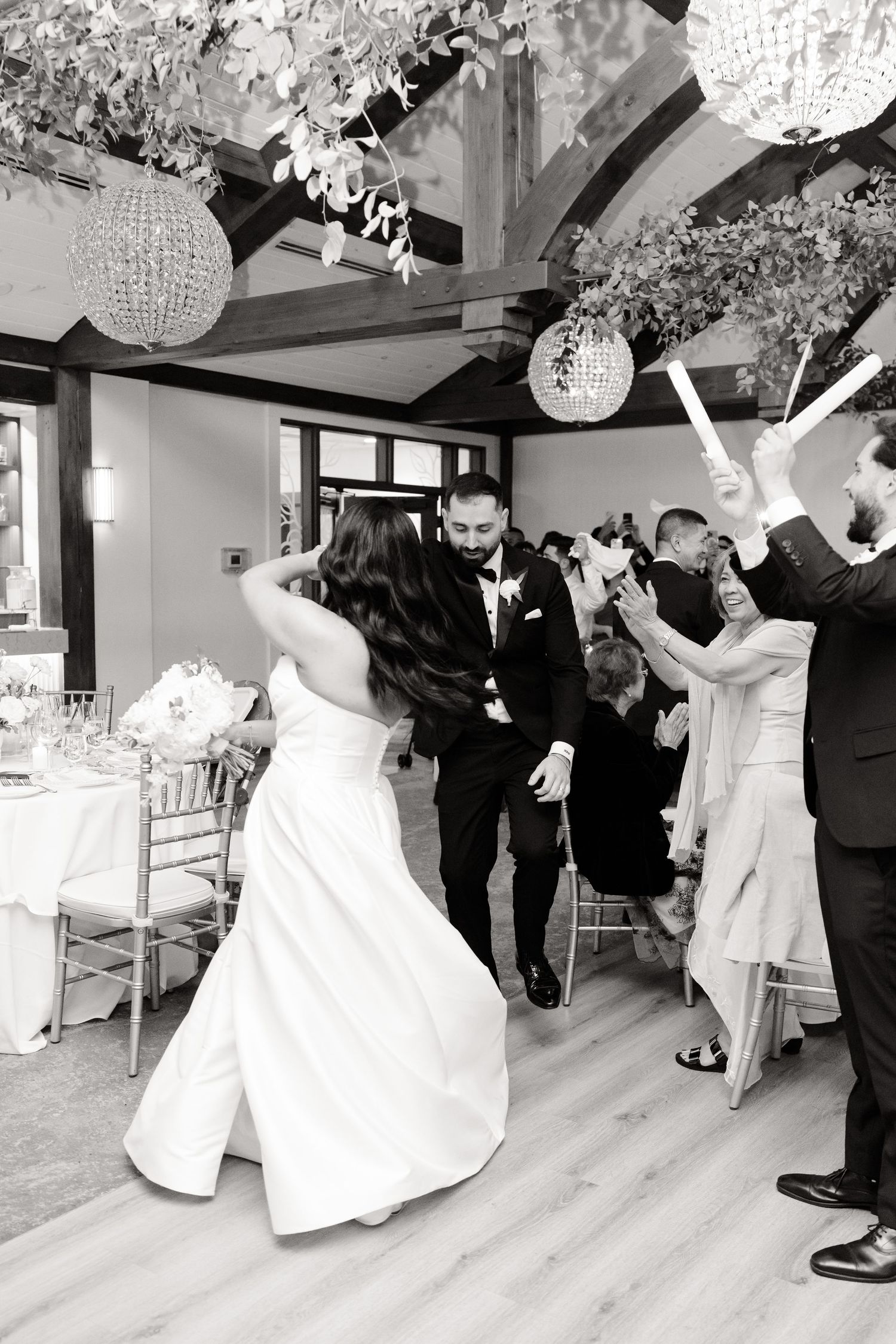 A joyous wedding reception moment captured in black and white under decorative lighting.