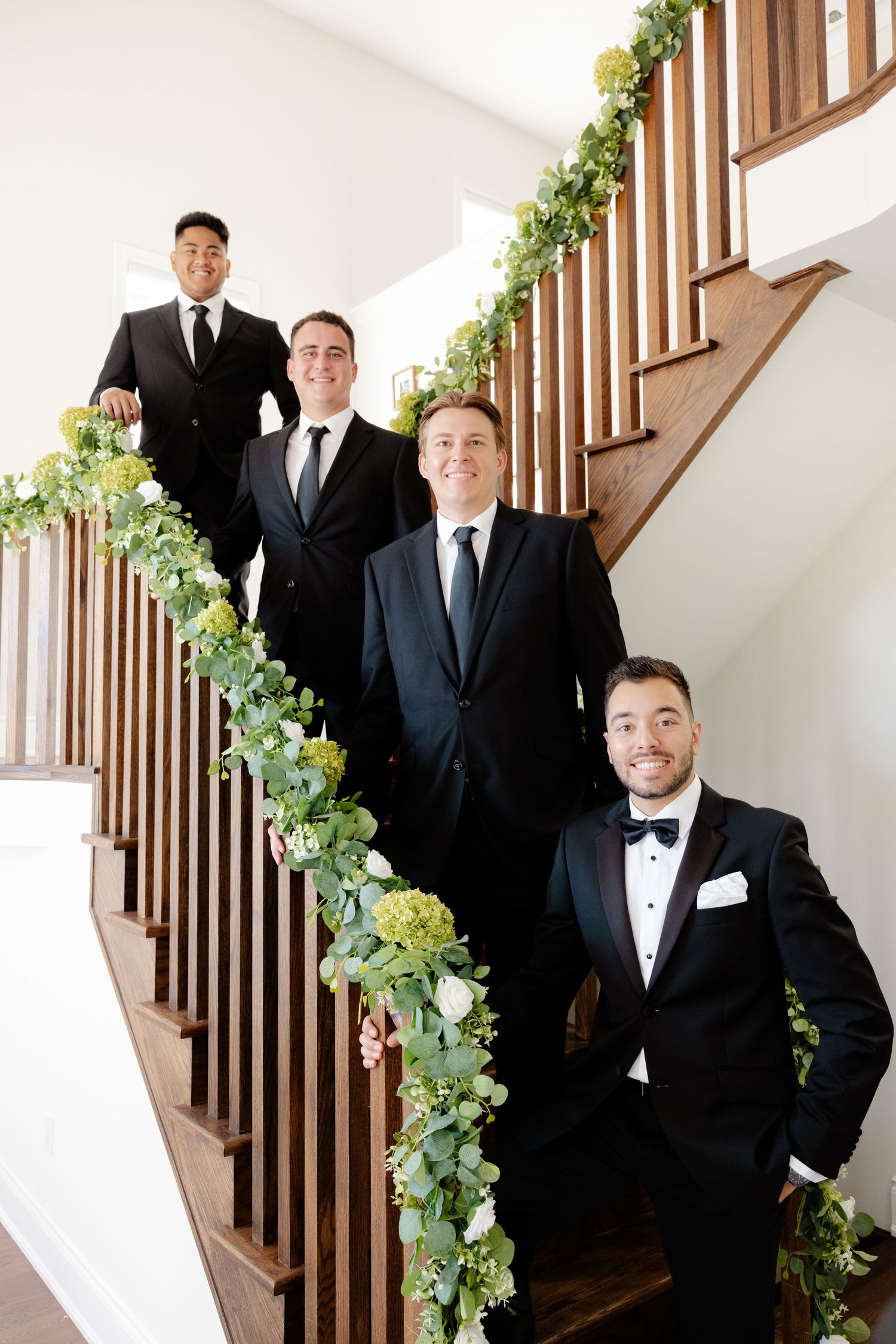 Four people in suits pose on staircase decorated with greenery garland.