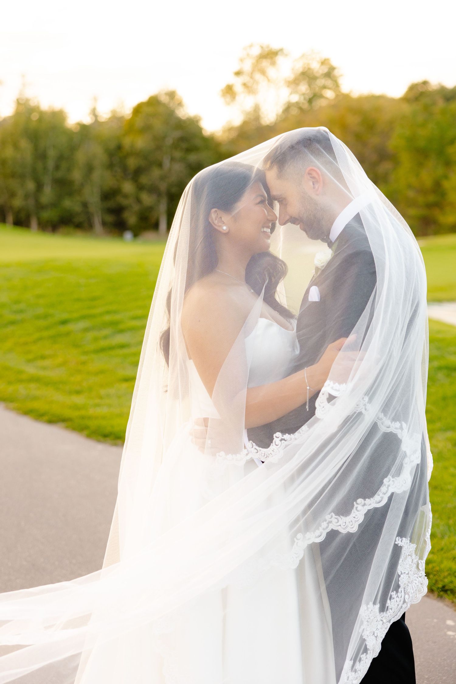 Romantic sunset wedding photo with couple embracing under a delicate lace veil.