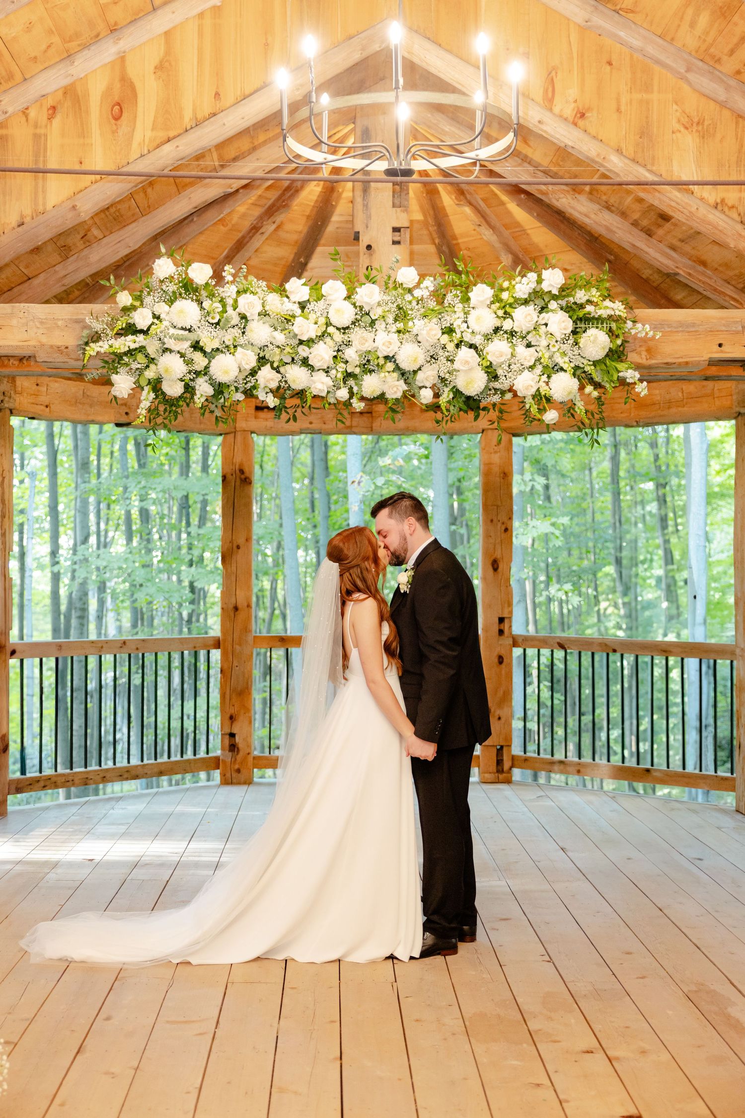 An intimate wedding moment captured in a wooden pavilion with elegant floral decor and forest views.