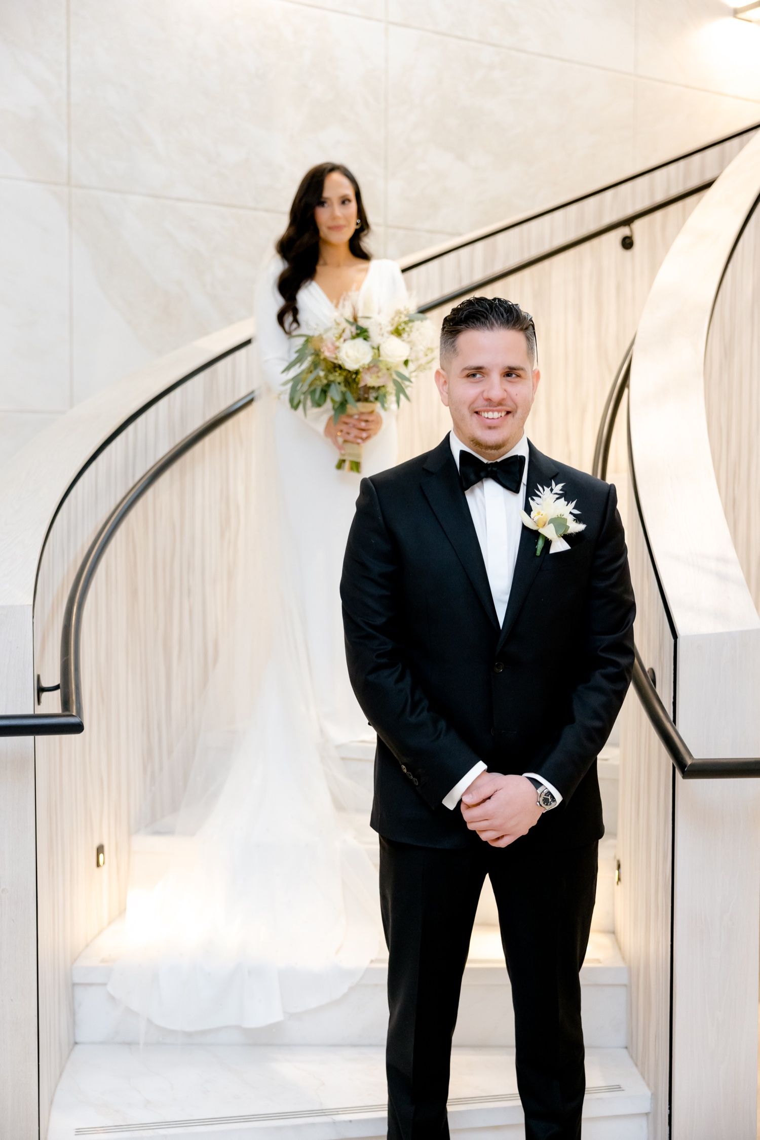 A romantic first look between newlyweds on an elegant white marble staircase.