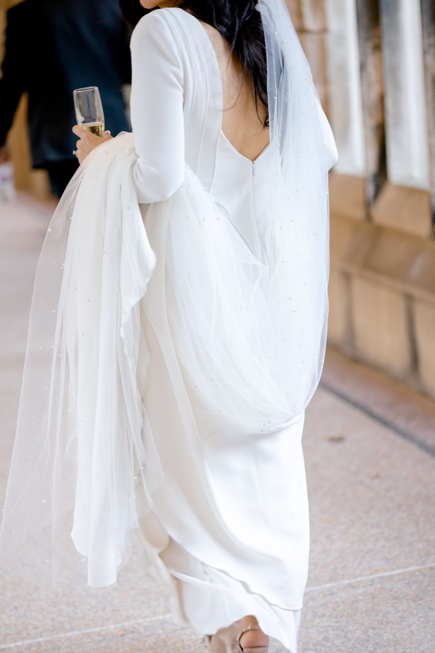 Elegant white wedding dress with long sleeves and flowing train shown from behind in an indoor corridor.
