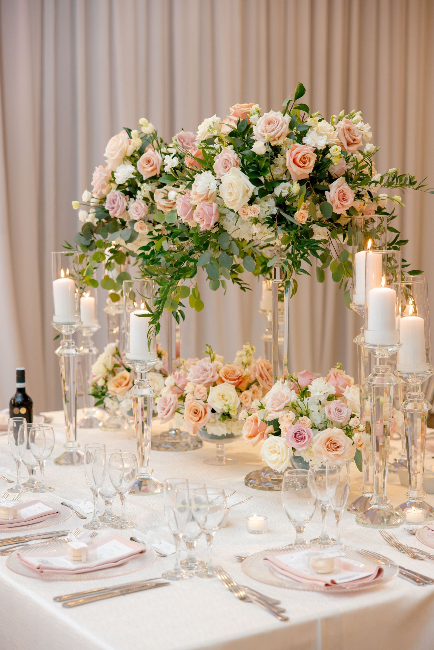 Dramatic tall wedding centerpiece with pink and cream roses above elegantly set dining table.