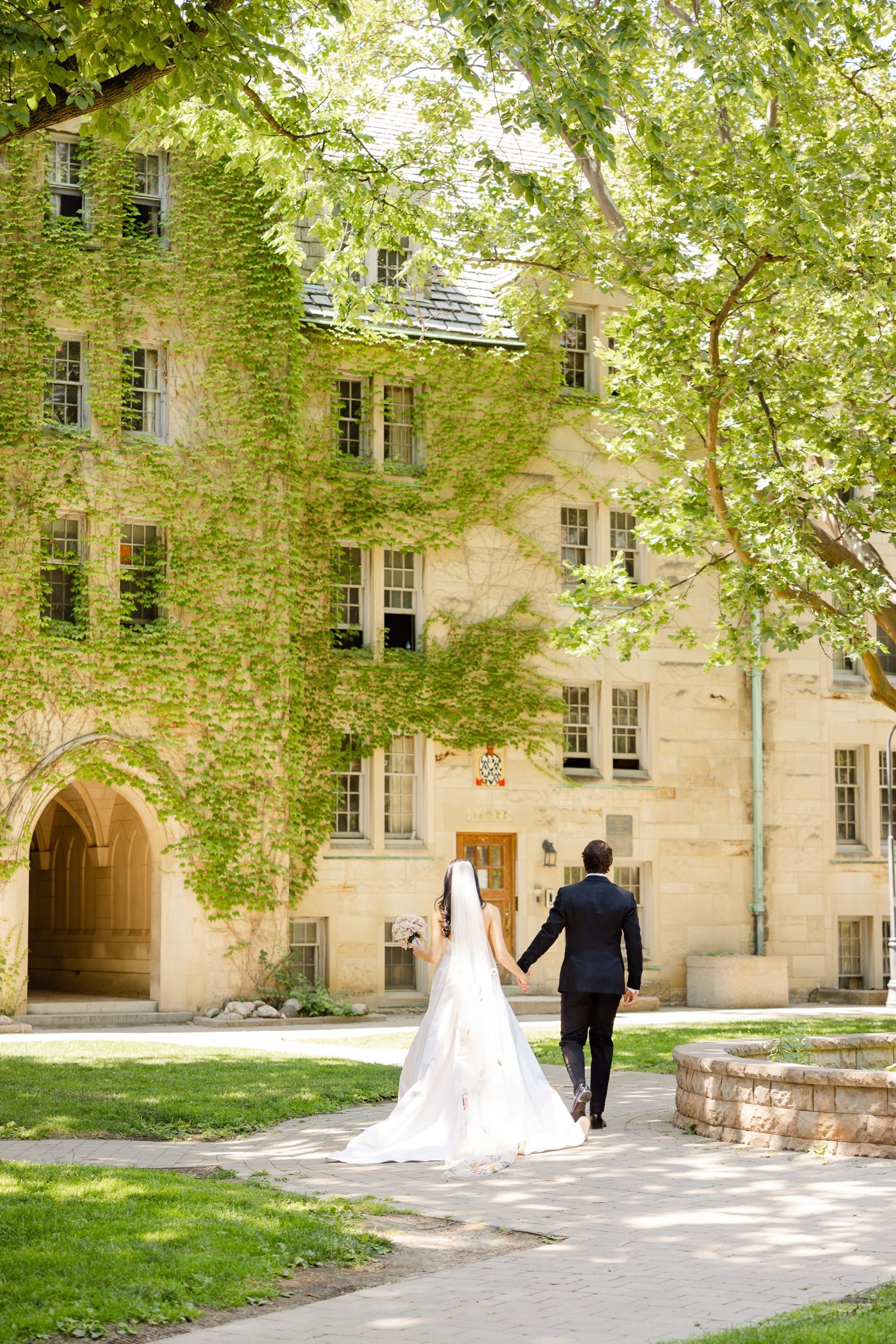 Couple walks toward ivy-covered stone building on their wedding day.