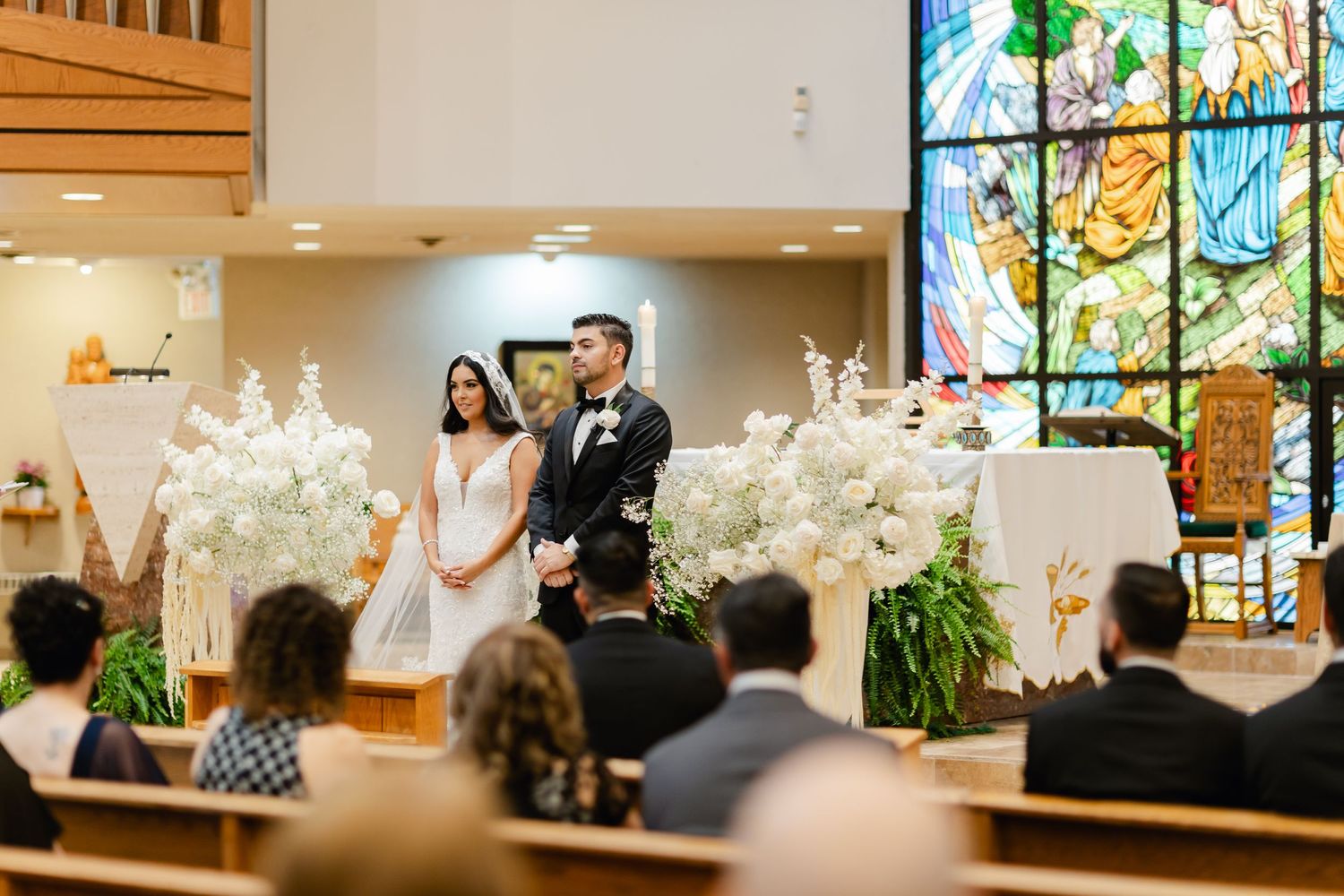 Wedding ceremony at modern church with stained glass and white floral decorations.