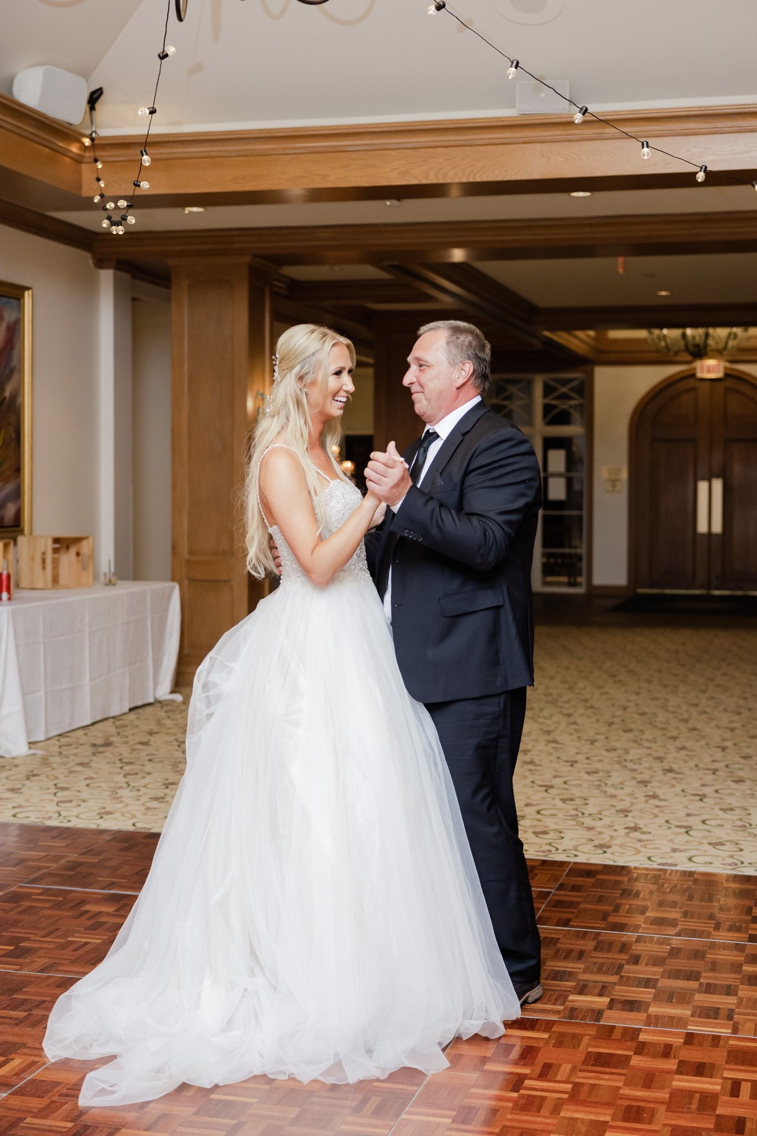 A special dance between a bride in a flowing white gown and a gentleman in a black suit at a wedding reception.
