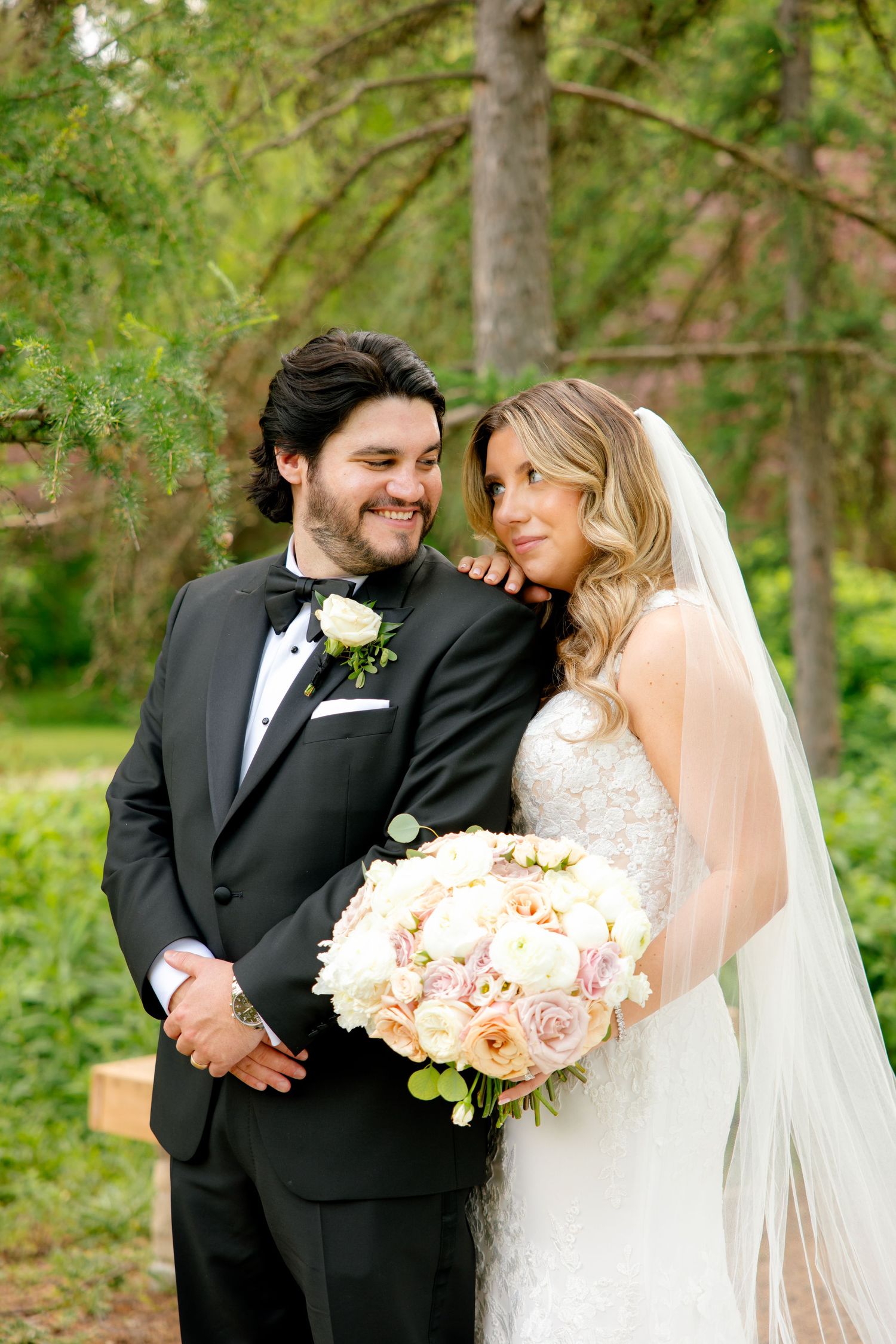 Elegant wedding portrait of a couple in a forest setting with a blush and cream floral bouquet.