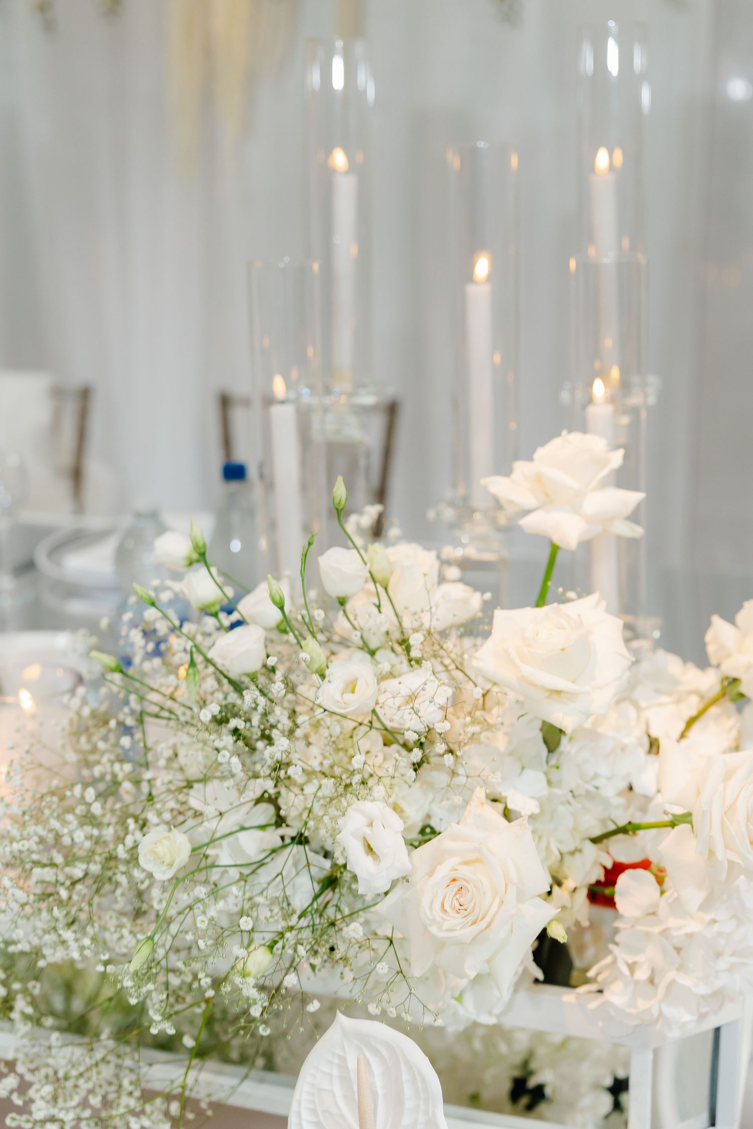 White roses and baby's breath floral arrangement with tall taper candles for an elegant wedding centerpiece.
