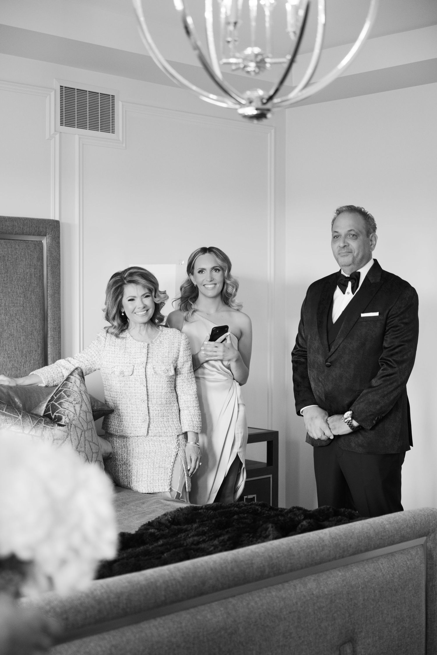 Wedding party guests in formal attire gathered beneath a modern chandelier in a stylish room.