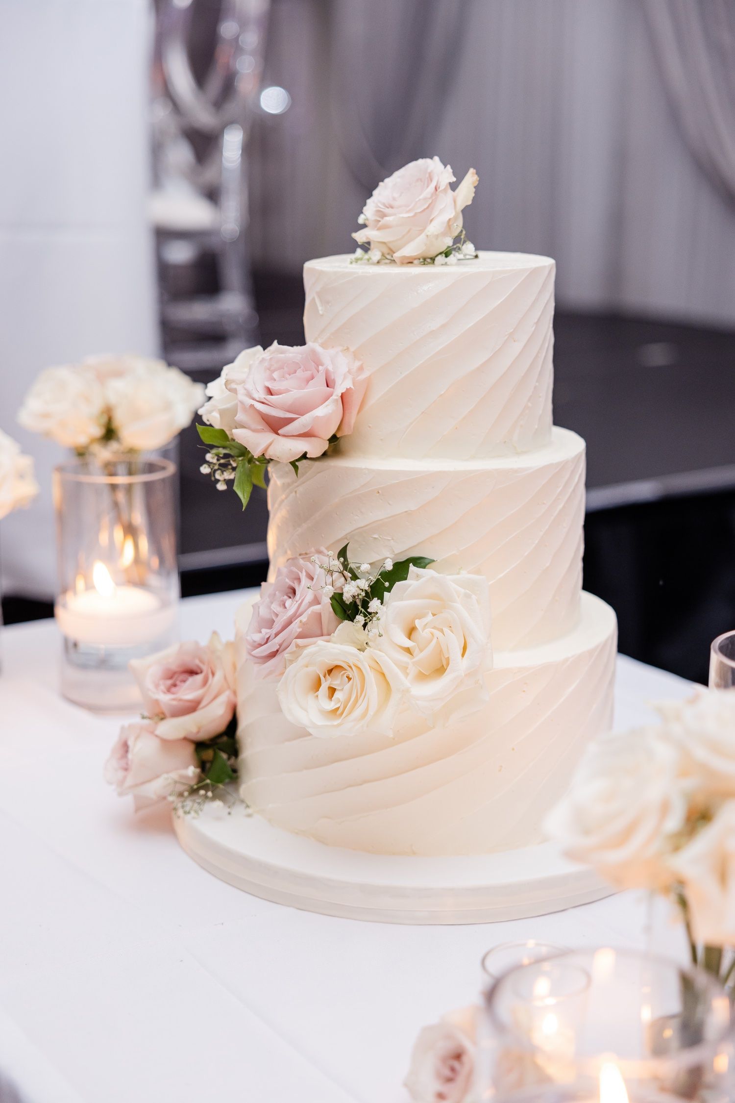 Three-tier white wedding cake decorated with blush roses and textured frosting design.
