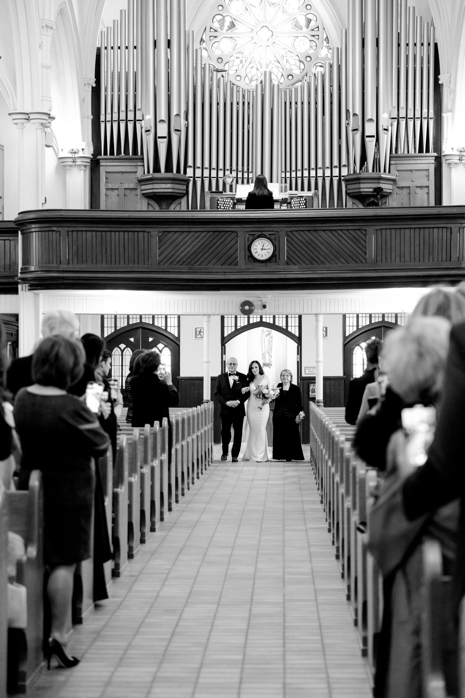 Black and white photo of wedding ceremony in church with grand pipe organ and guests in pews.
