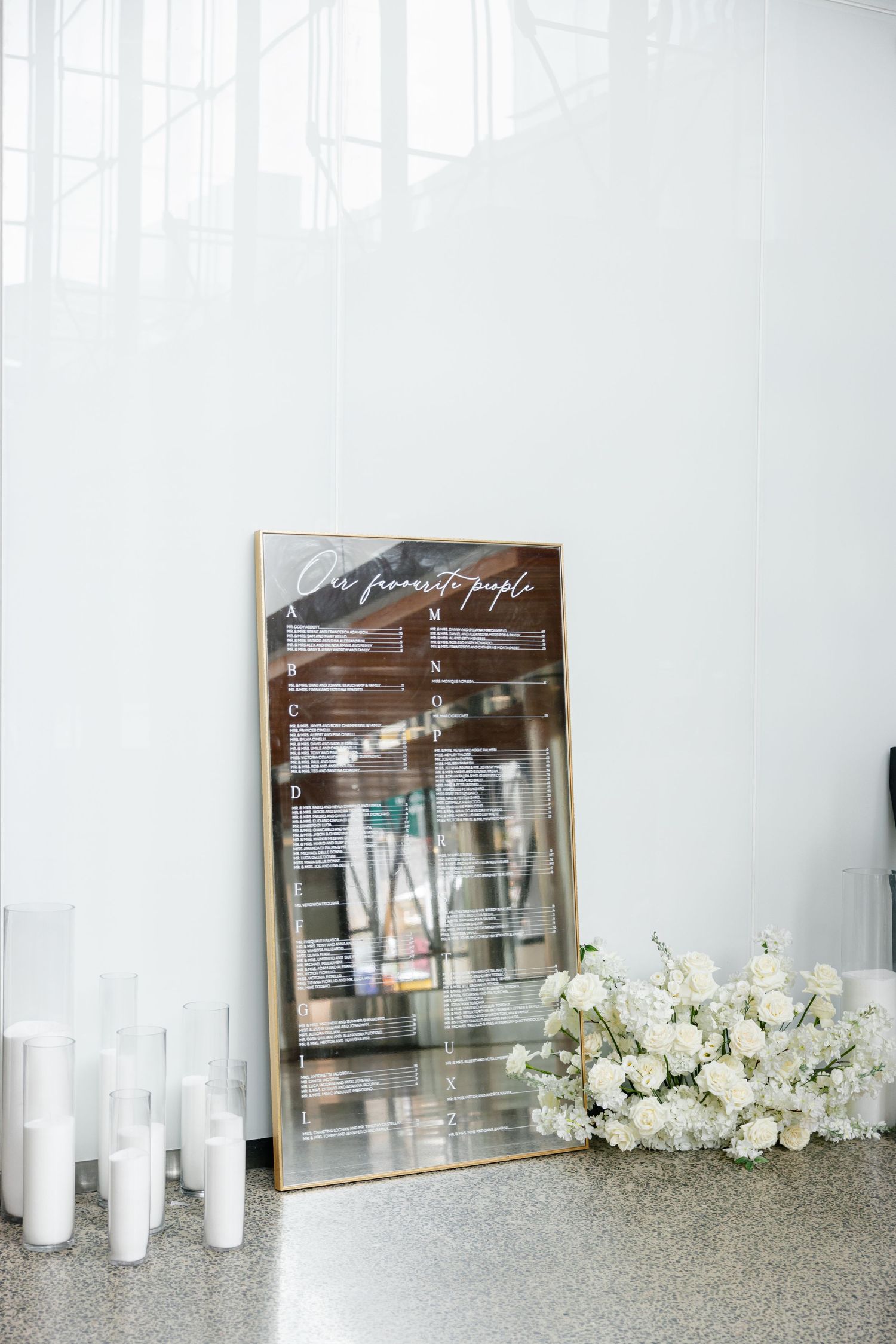 Mirror with calligraphy text displayed against white wall with pillar candles and white floral arrangements.