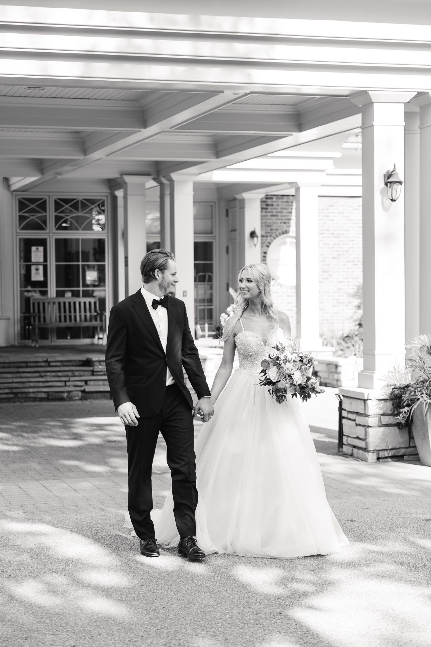 Black and white portrait of newlyweds holding hands under an elegant portico entrance.