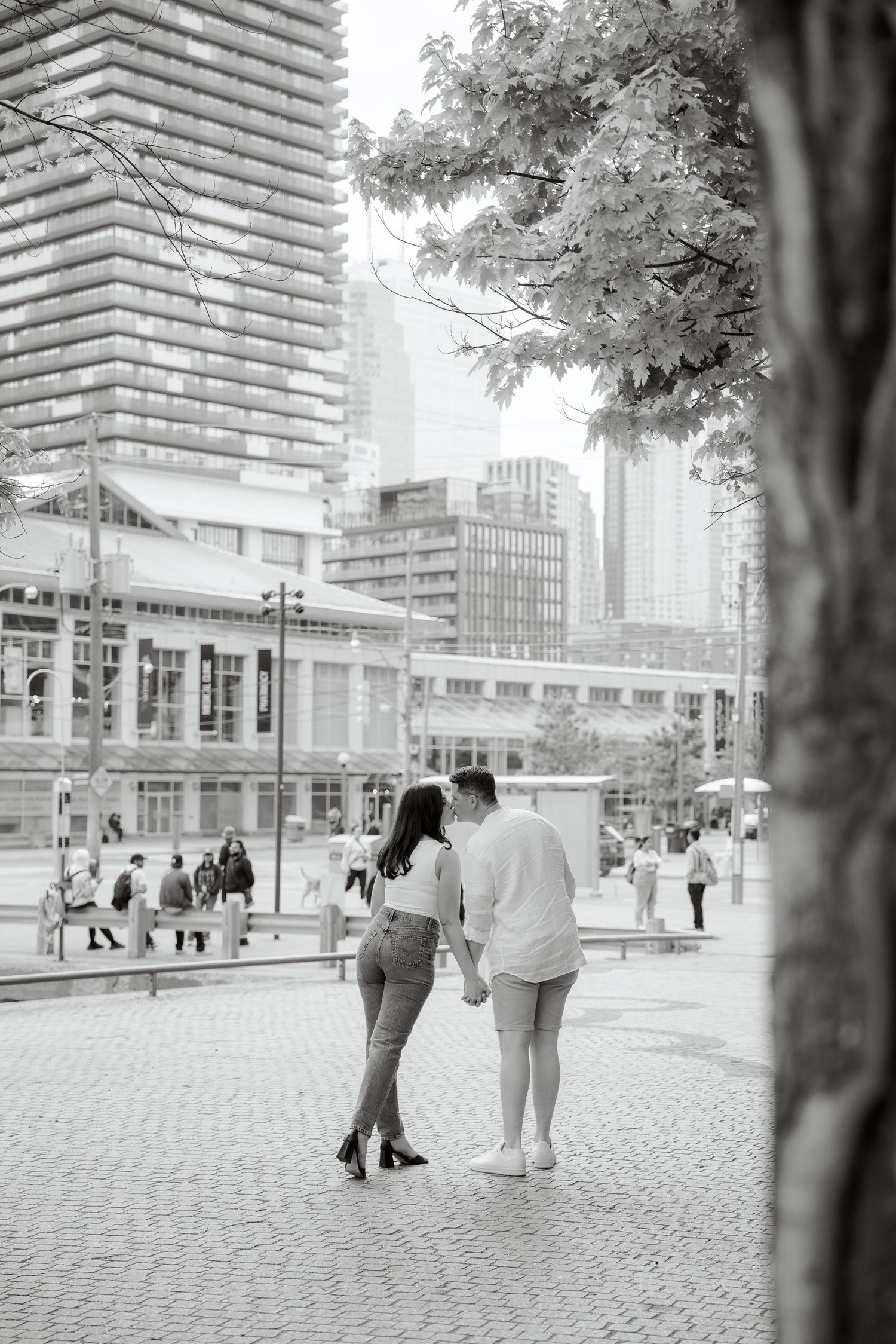 A black and white photo of a couple walking near modern buildings in downtown Toronto.