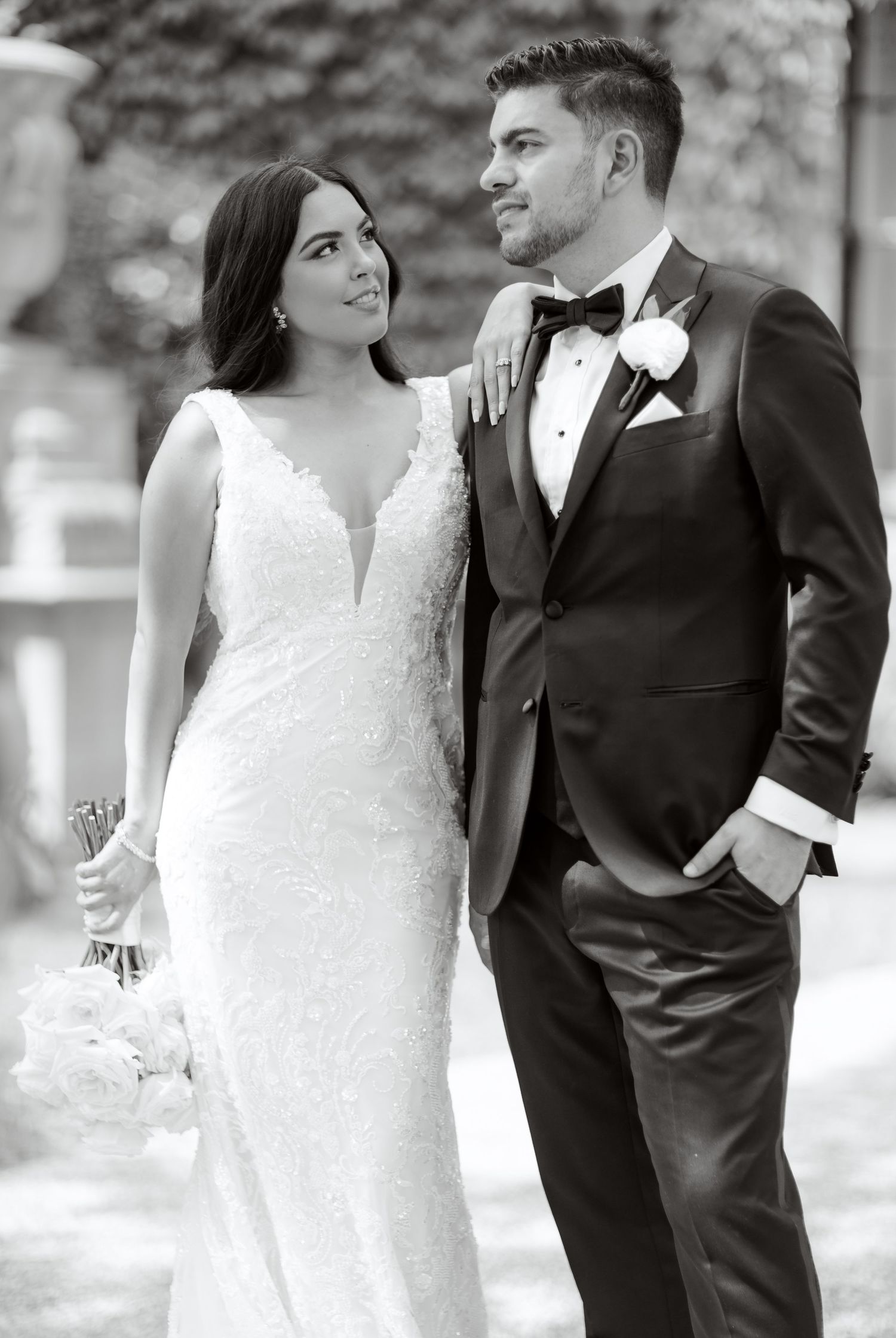 Black and white portrait of newlyweds sharing an intimate moment against an ivy wall backdrop.