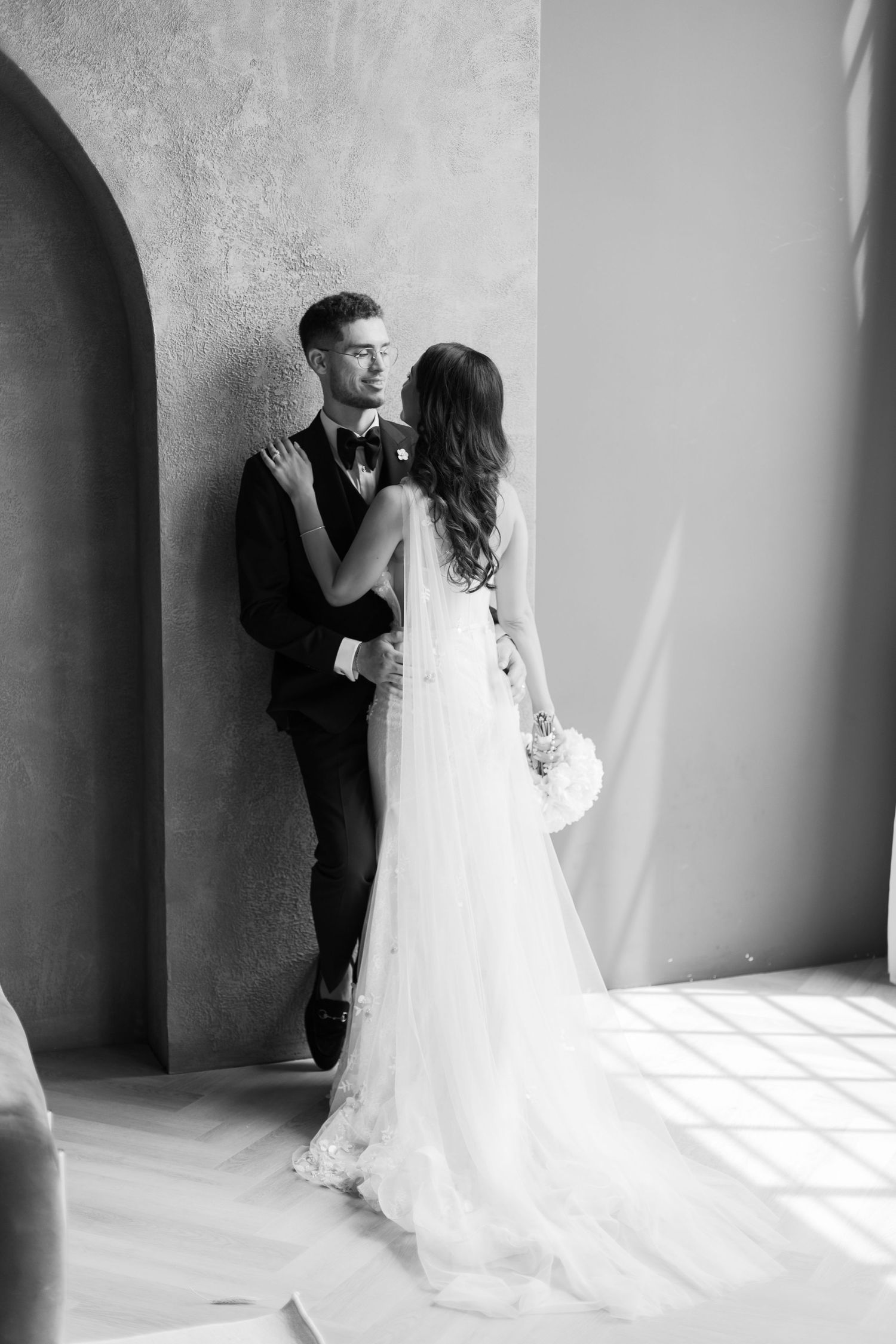 Black and white portrait of wedding couple posed against concrete arch with natural light.
