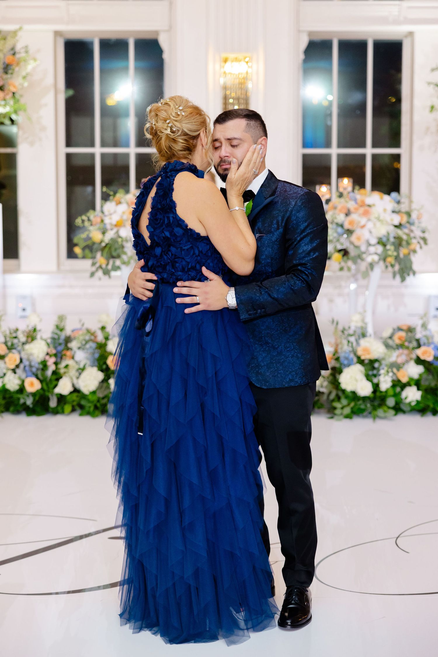 Couple dancing in navy blue and black formal attire at an elegant wedding reception.