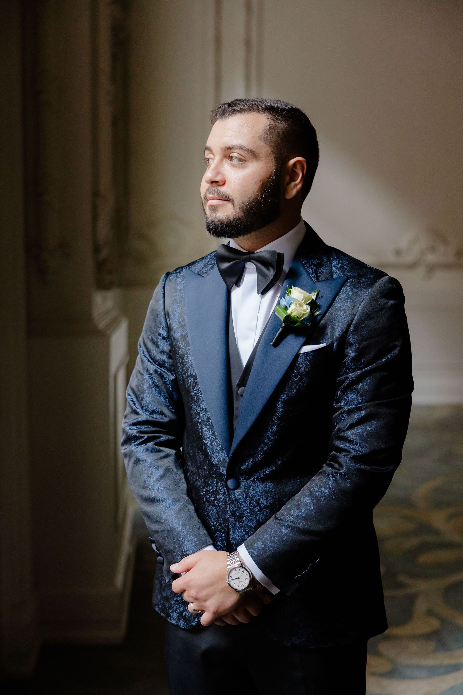 Groom in dark patterned suit stands confidently in formal portrait session.